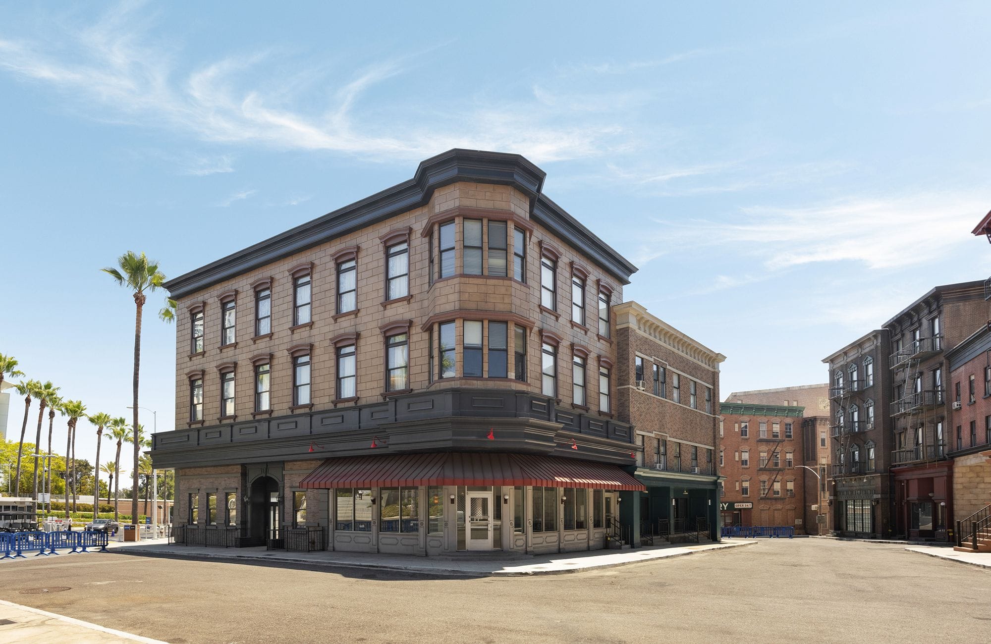 A three-story corner building with an old-style brick facade, palm trees, and other buildings under a blue sky.