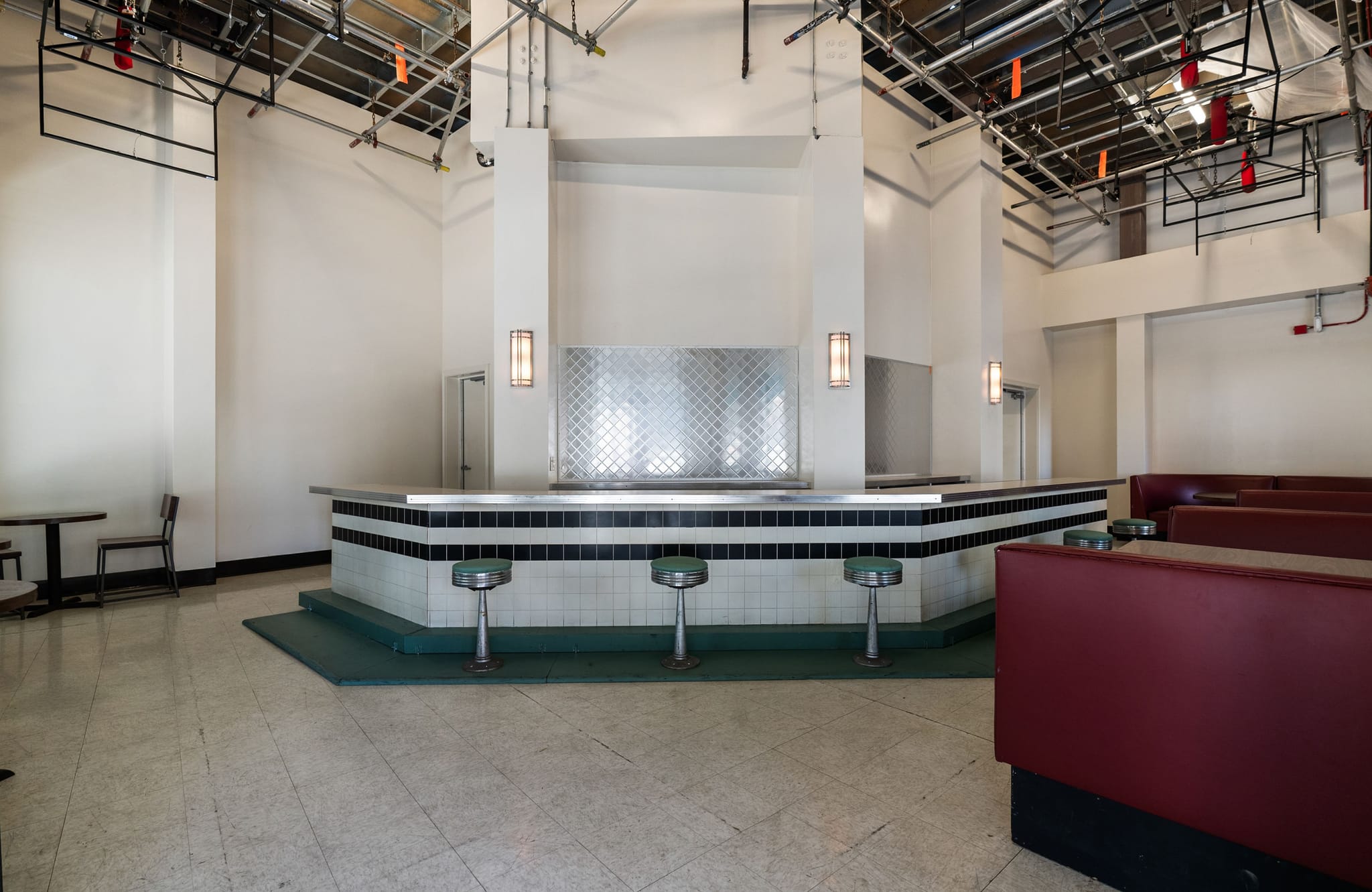 Empty retro diner set with a counter, green stools, red booths, and exposed studio rigging above.