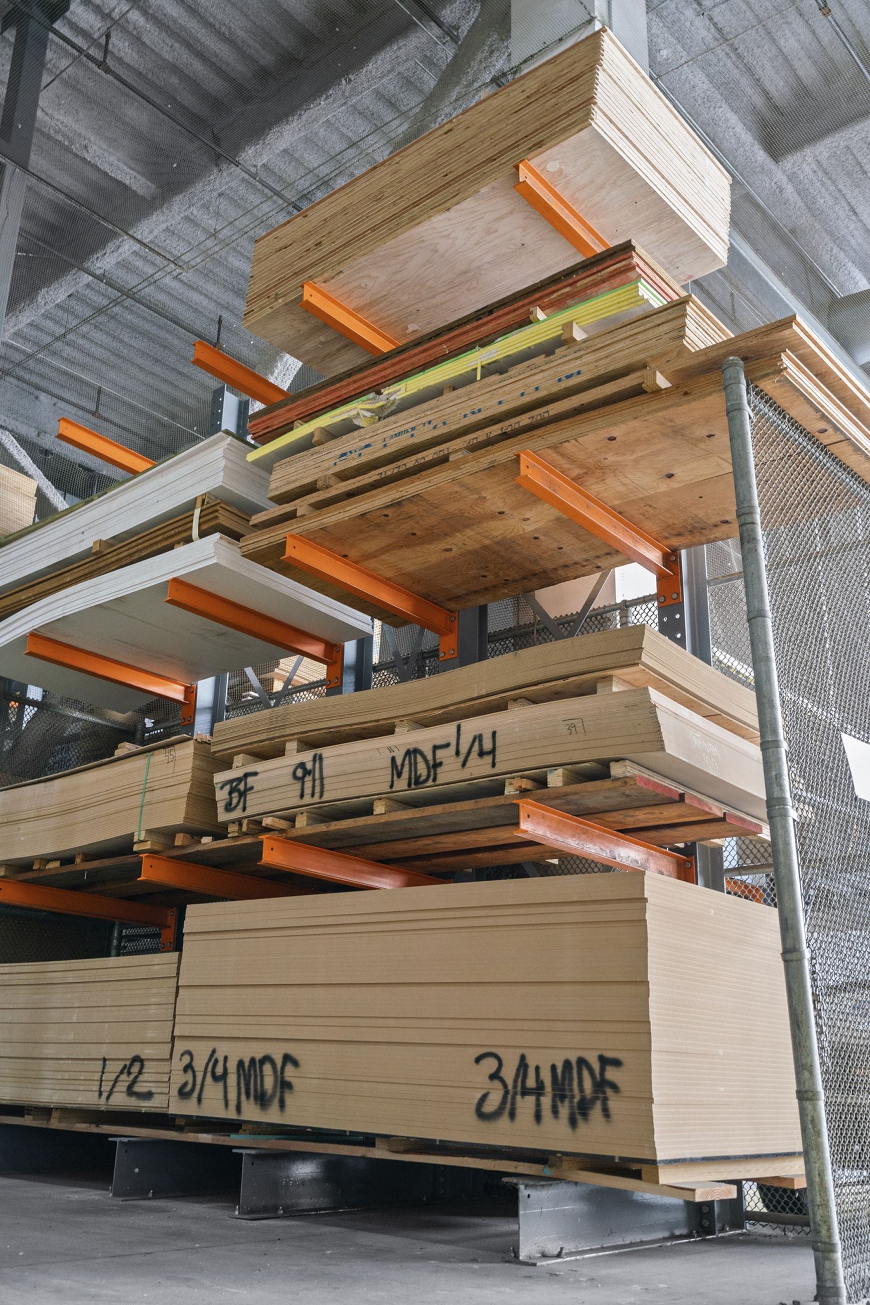 Various wood and MDF panels stacked on orange metal shelves in a warehouse.