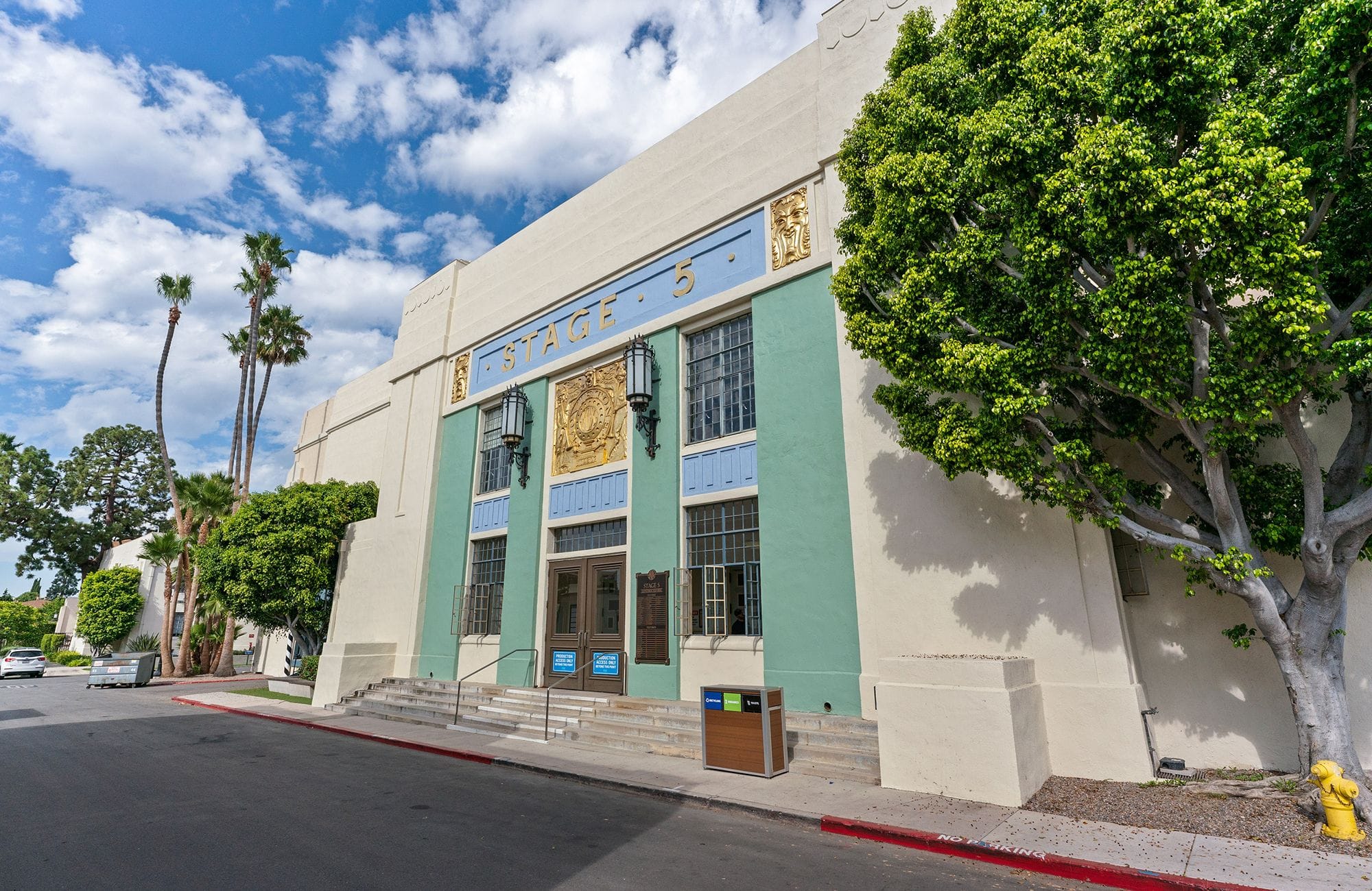 A cream and blue building with "STAGE 5" on its facade, flanked by trees under a cloudy sky.
