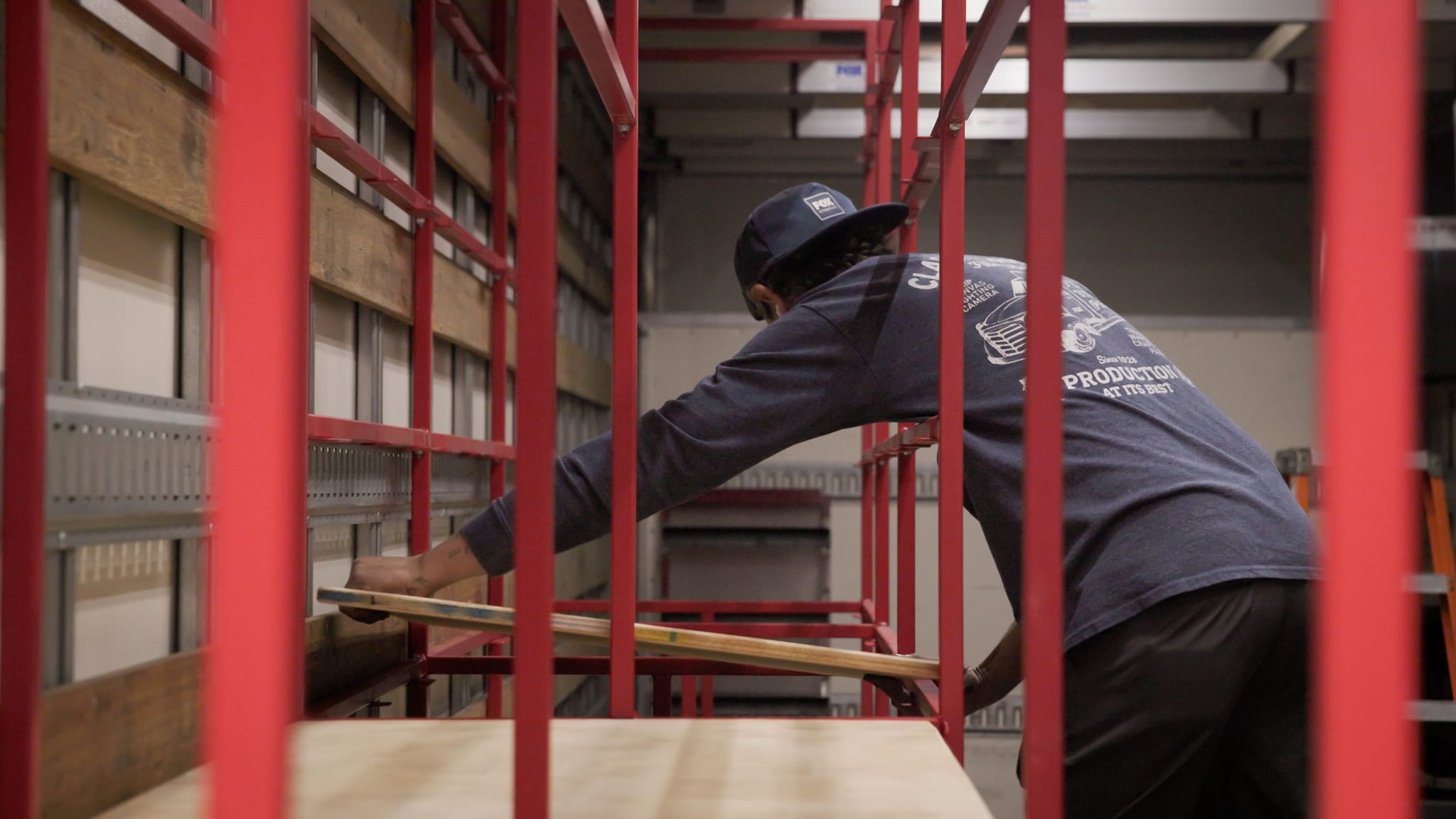 A person places wooden planks inside a truck or storage unit, seen through red bars.