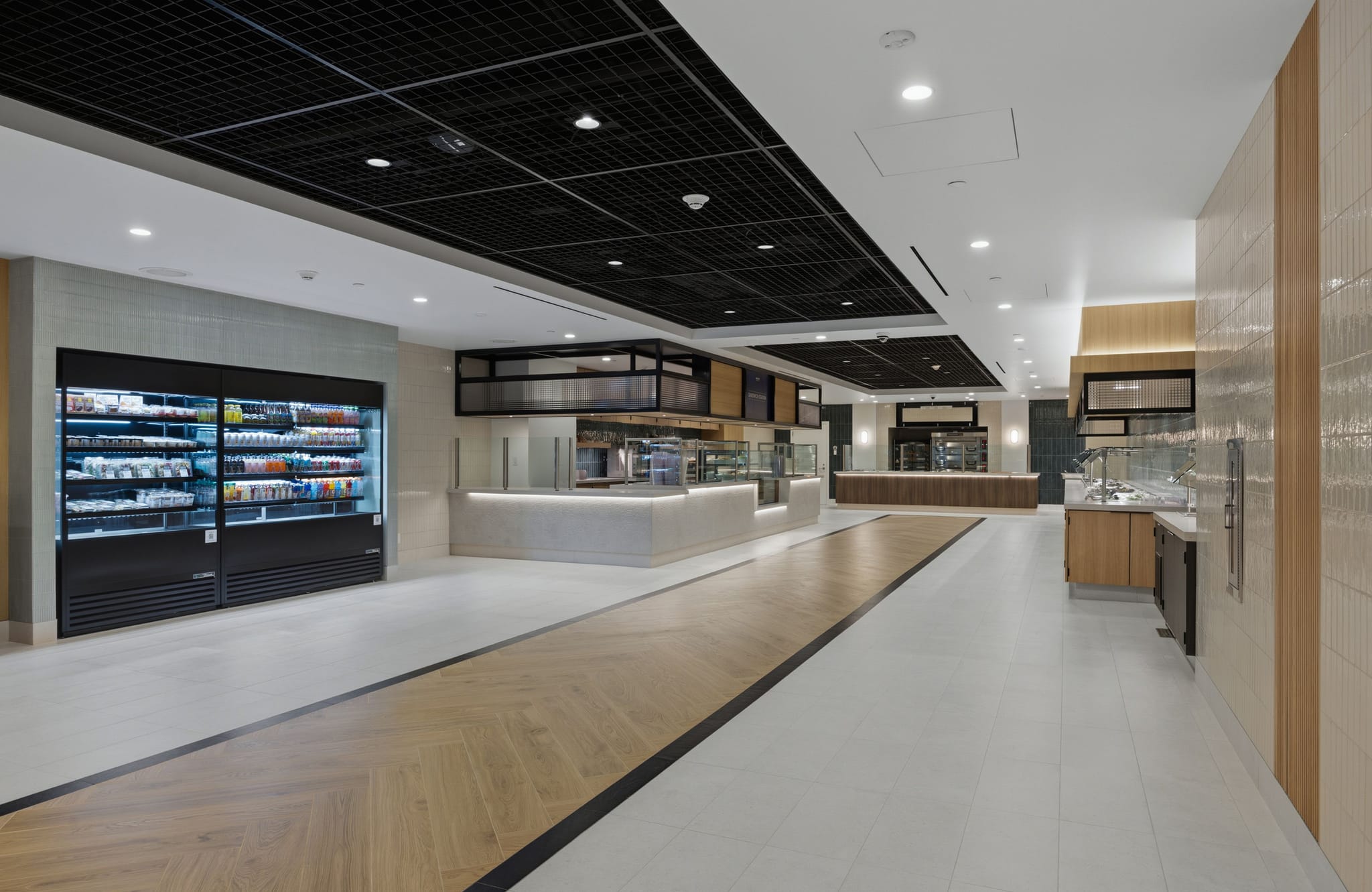 Modern, empty cafeteria with a large refrigerated grab-and-go display and various food serving counters.