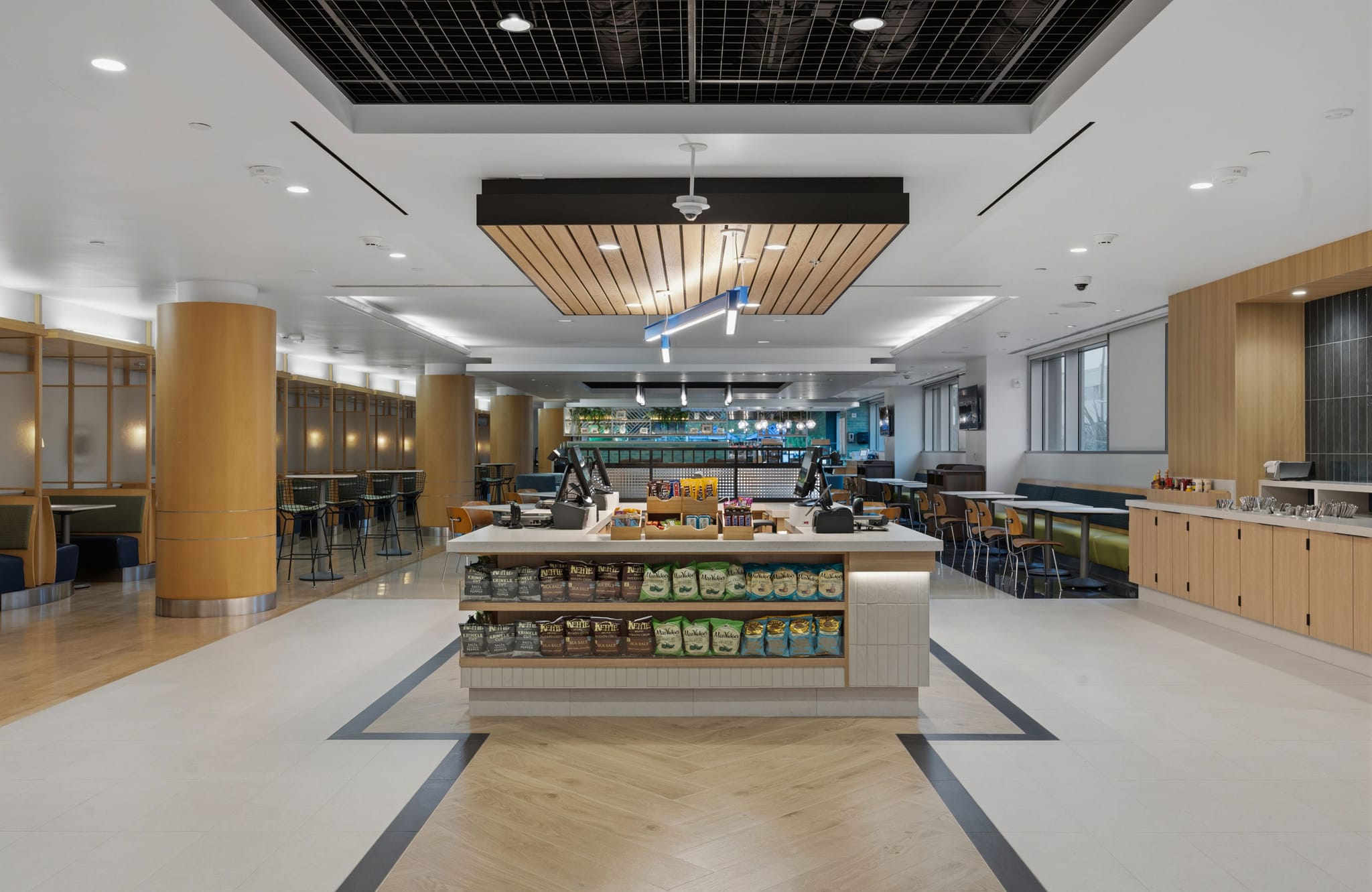Modern cafeteria interior with a central snack display, booth seating, and wood paneling.