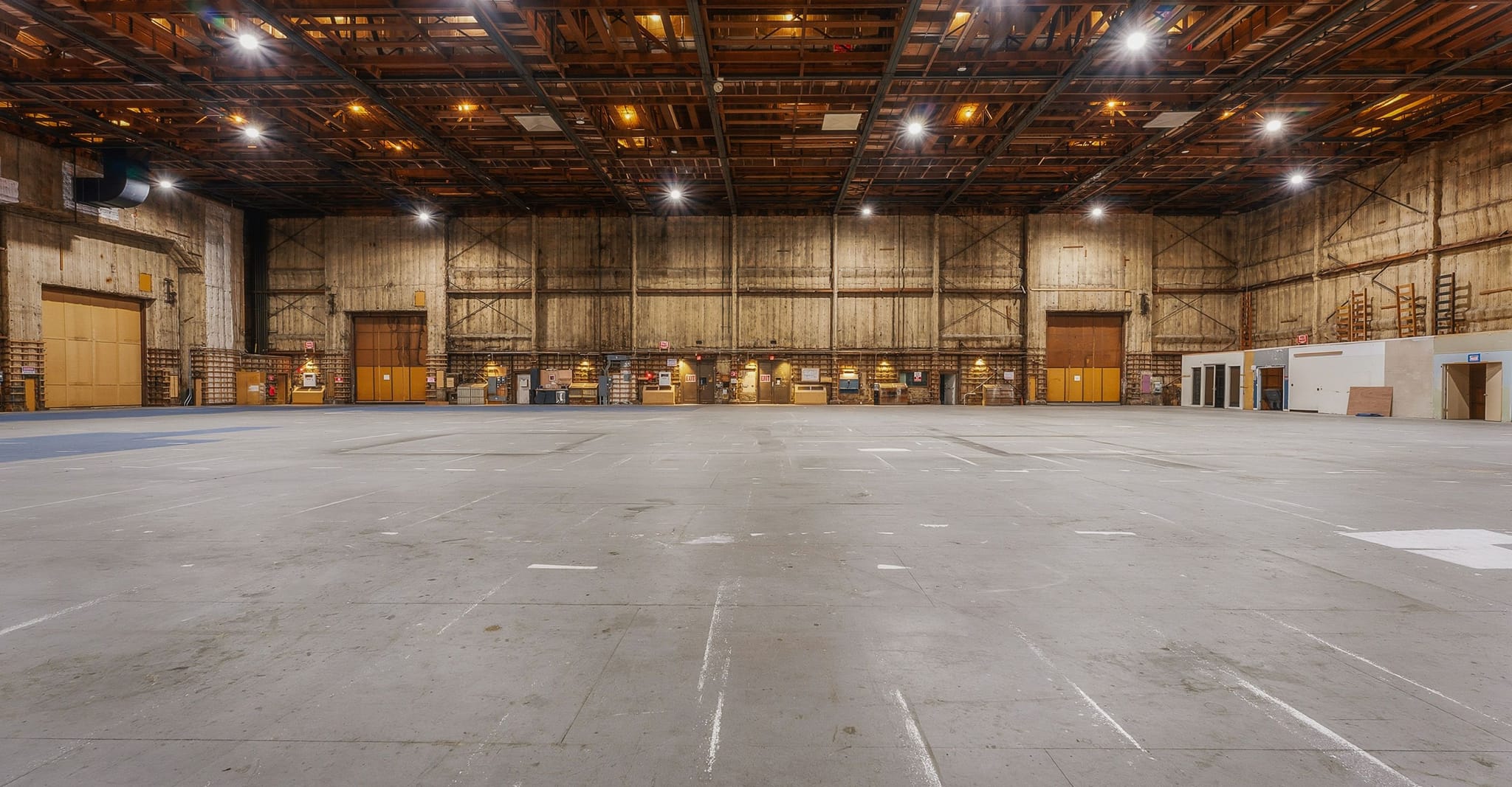 Empty industrial warehouse with a concrete floor, high ceilings, and bright lighting.