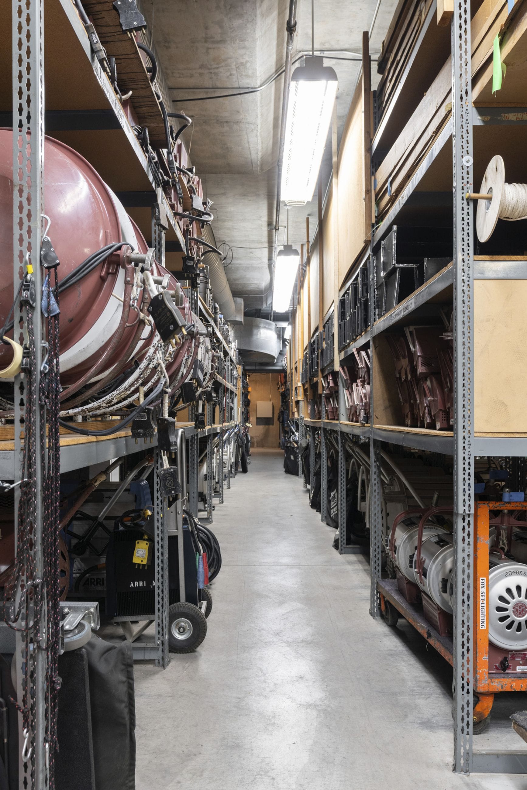 A long aisle in a warehouse filled with film and lighting production equipment.