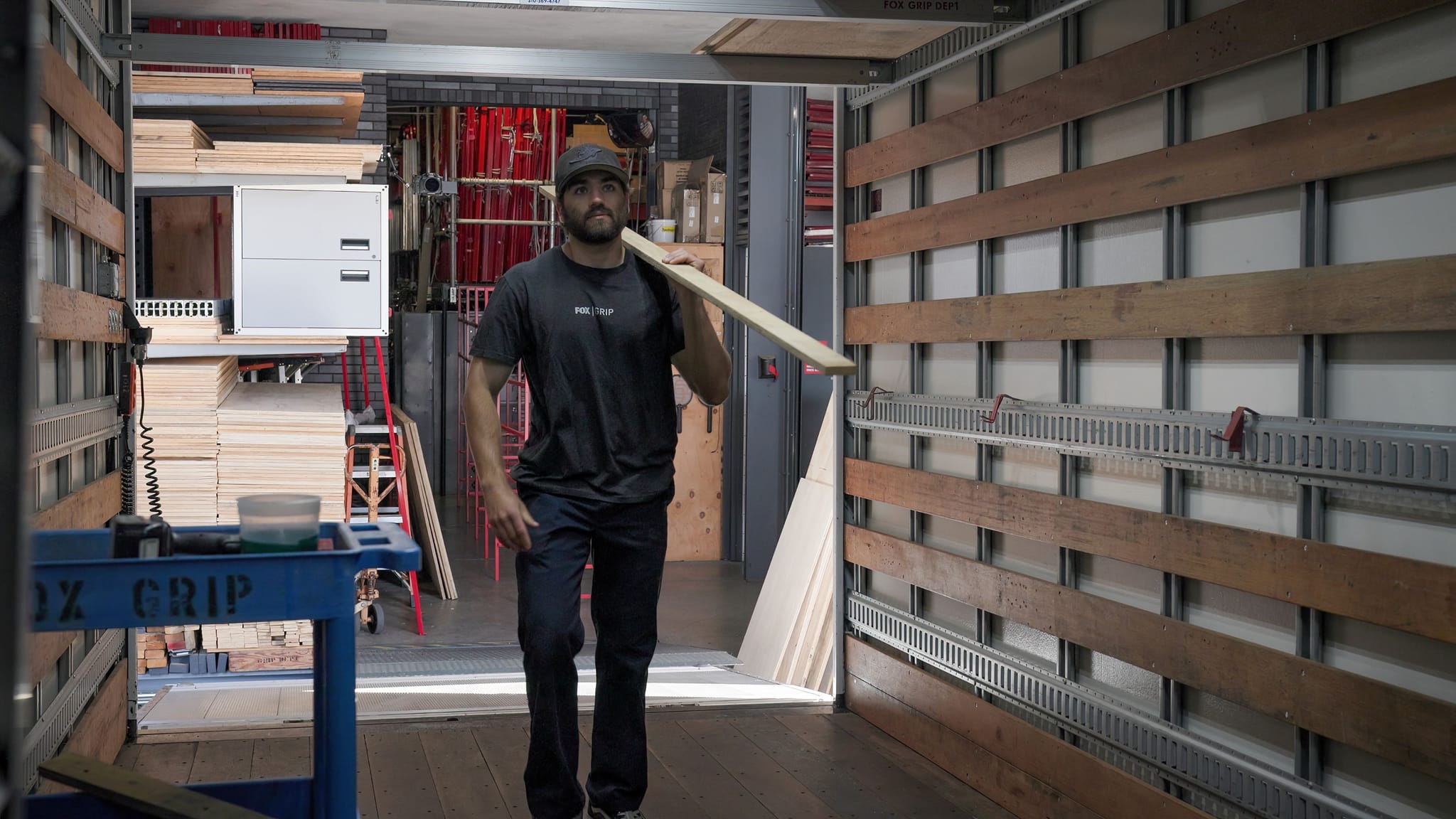 A man carries a wooden board inside a truck or trailer.