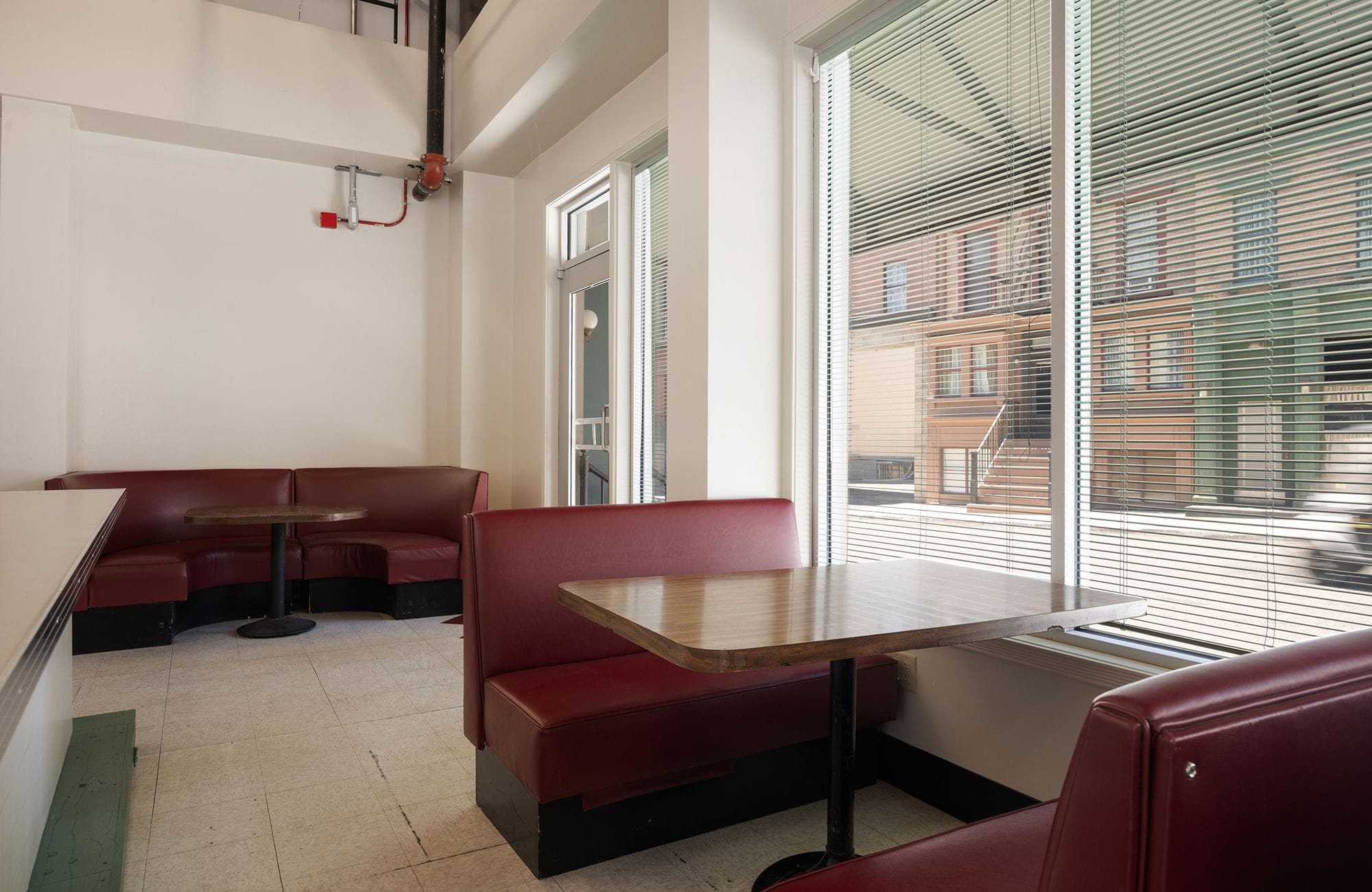 Empty diner with red booths and wooden tables, with large windows looking out onto a street with buildings.