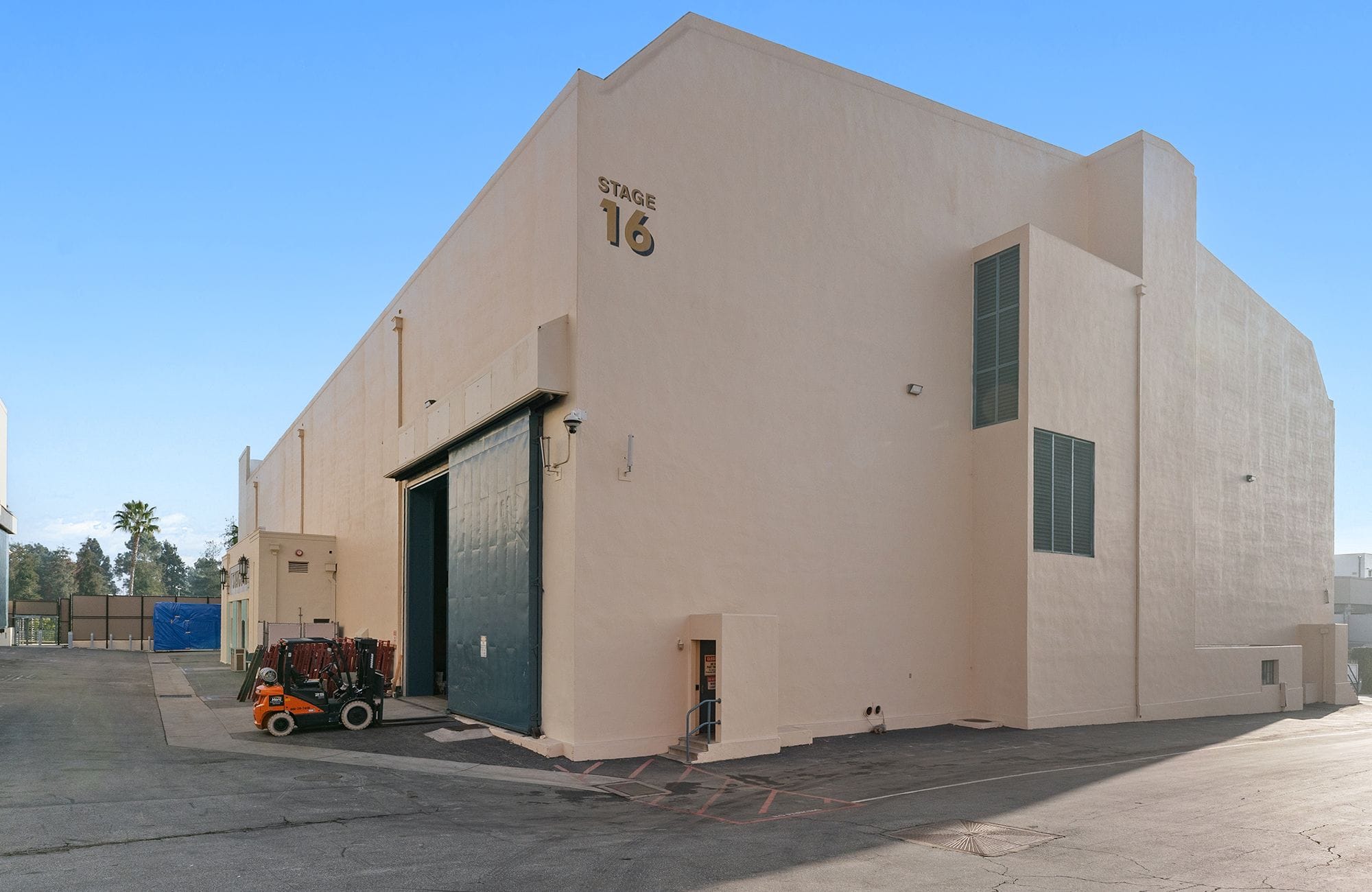 A large, light-colored building labeled "STAGE 16" with a huge sliding door and a forklift parked outside.