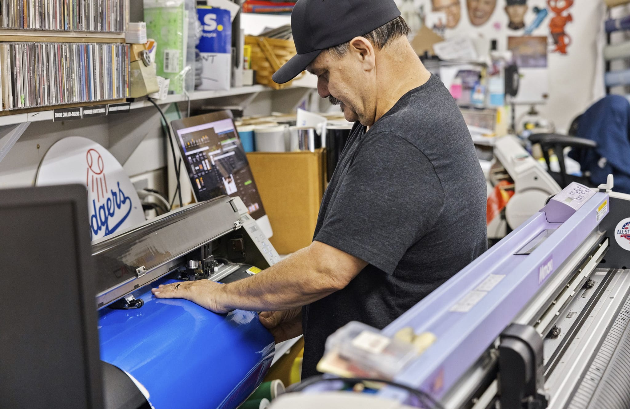 Man feeding blue vinyl into a large format cutting machine.