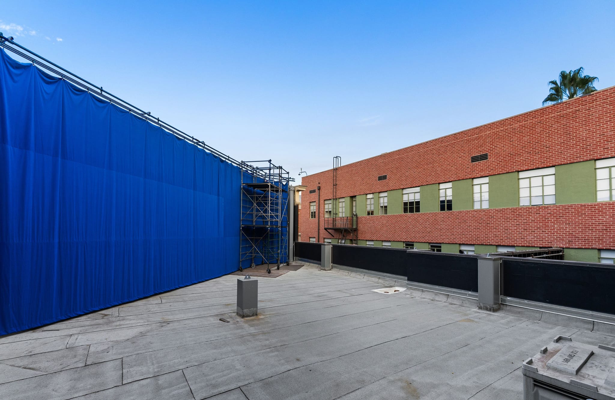 A rooftop with a large blue screen on the left and a brick building with green sections on the right.