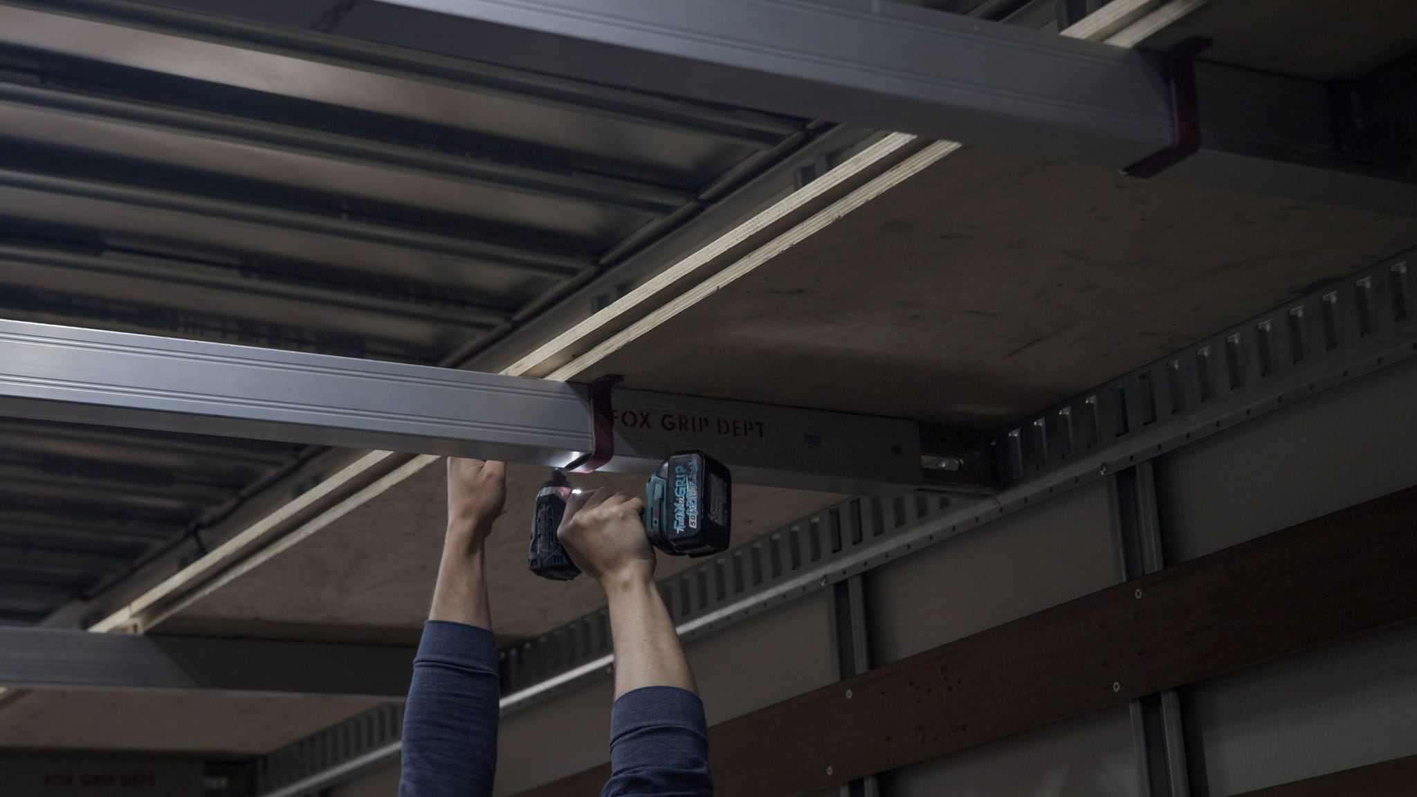Hands using a drill to install a metal beam inside a cargo trailer.