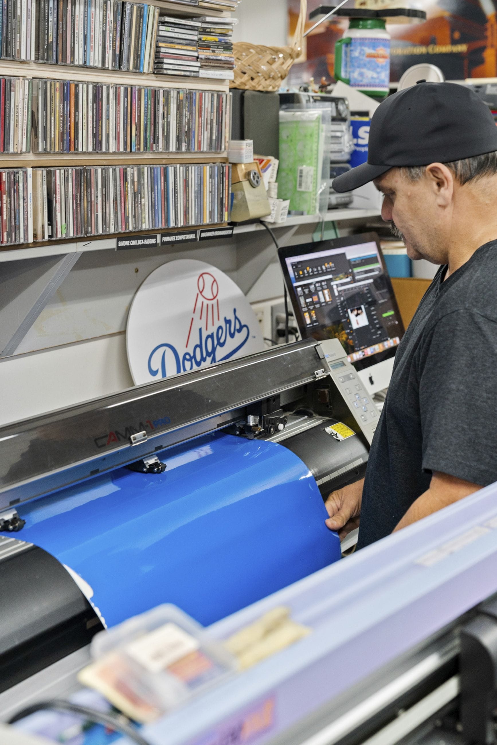A man feeds a sheet of blue material into a cutting machine, looking at a computer screen.