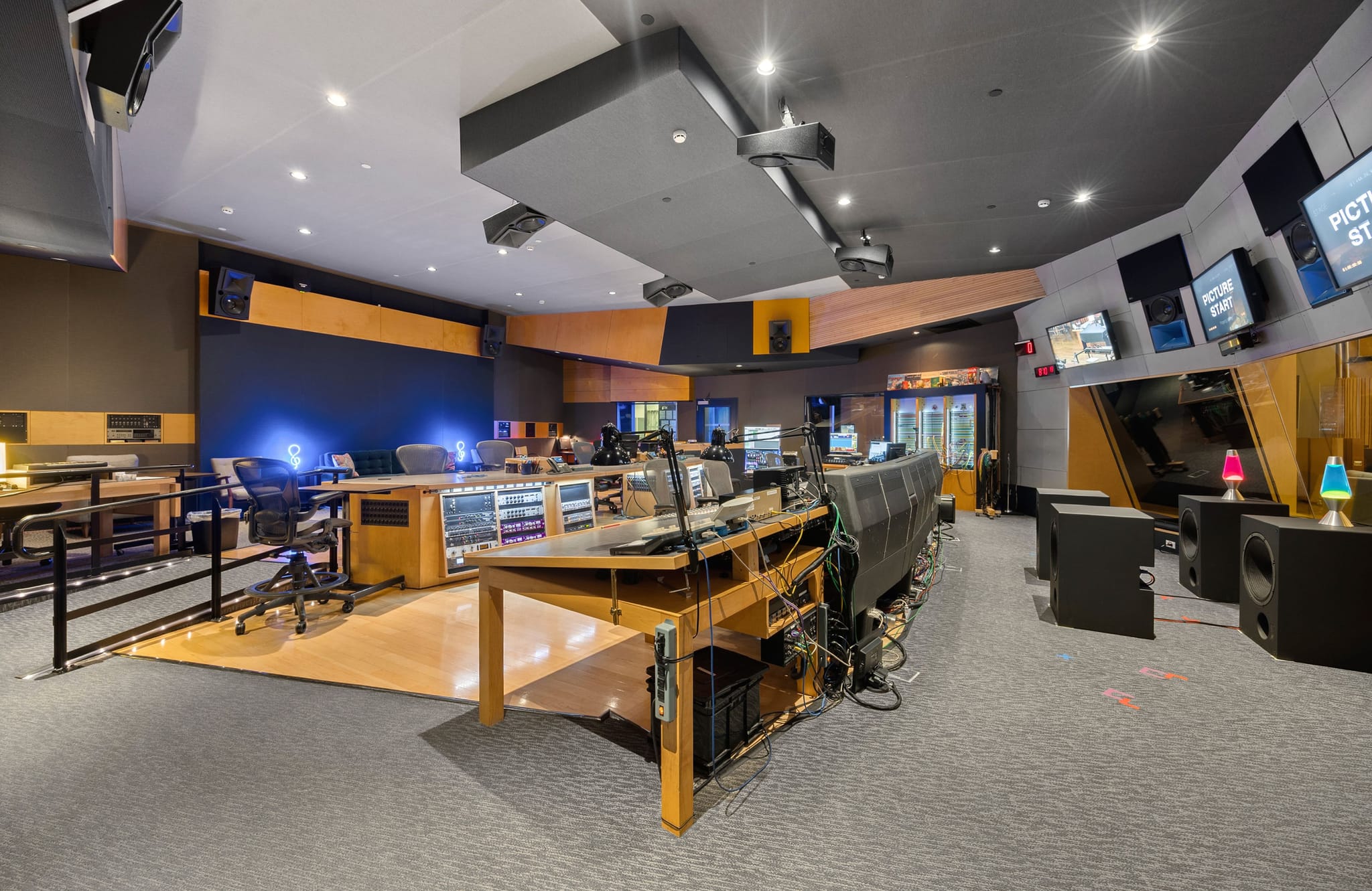 A modern, professional audio and video production studio with multiple workstations, screens, and audio equipment.