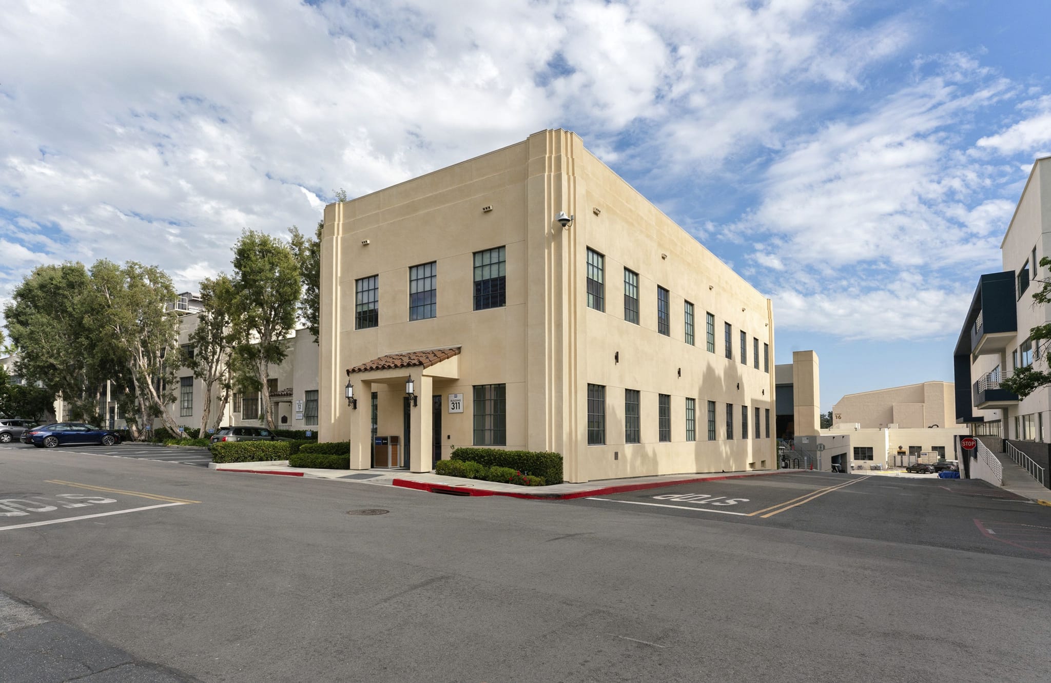 A two-story, light-colored Art Deco style building with a tiled entrance canopy, seen from a street under a cloudy sky.