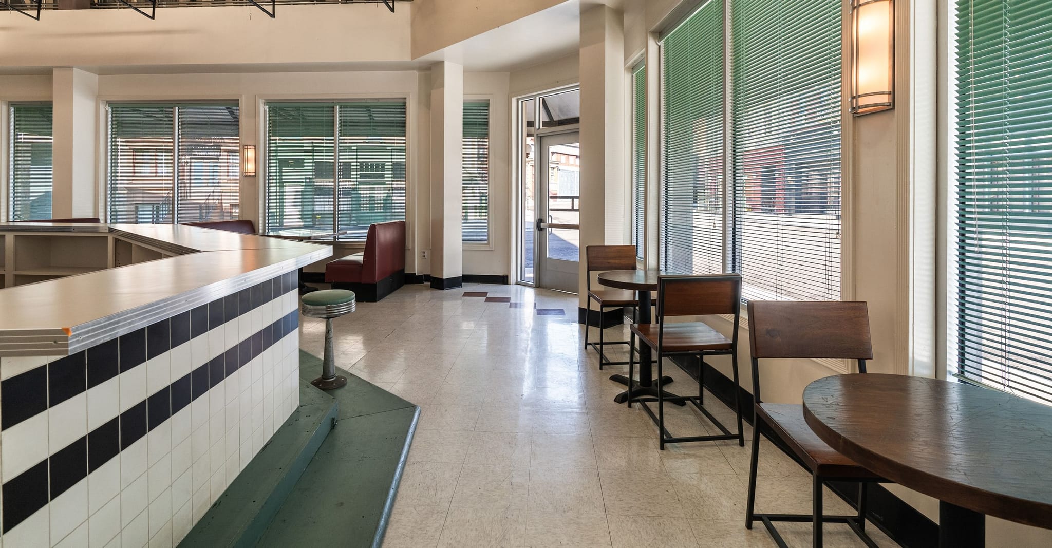 Empty retro diner interior with a black and white tiled counter, red booths, and wooden tables.