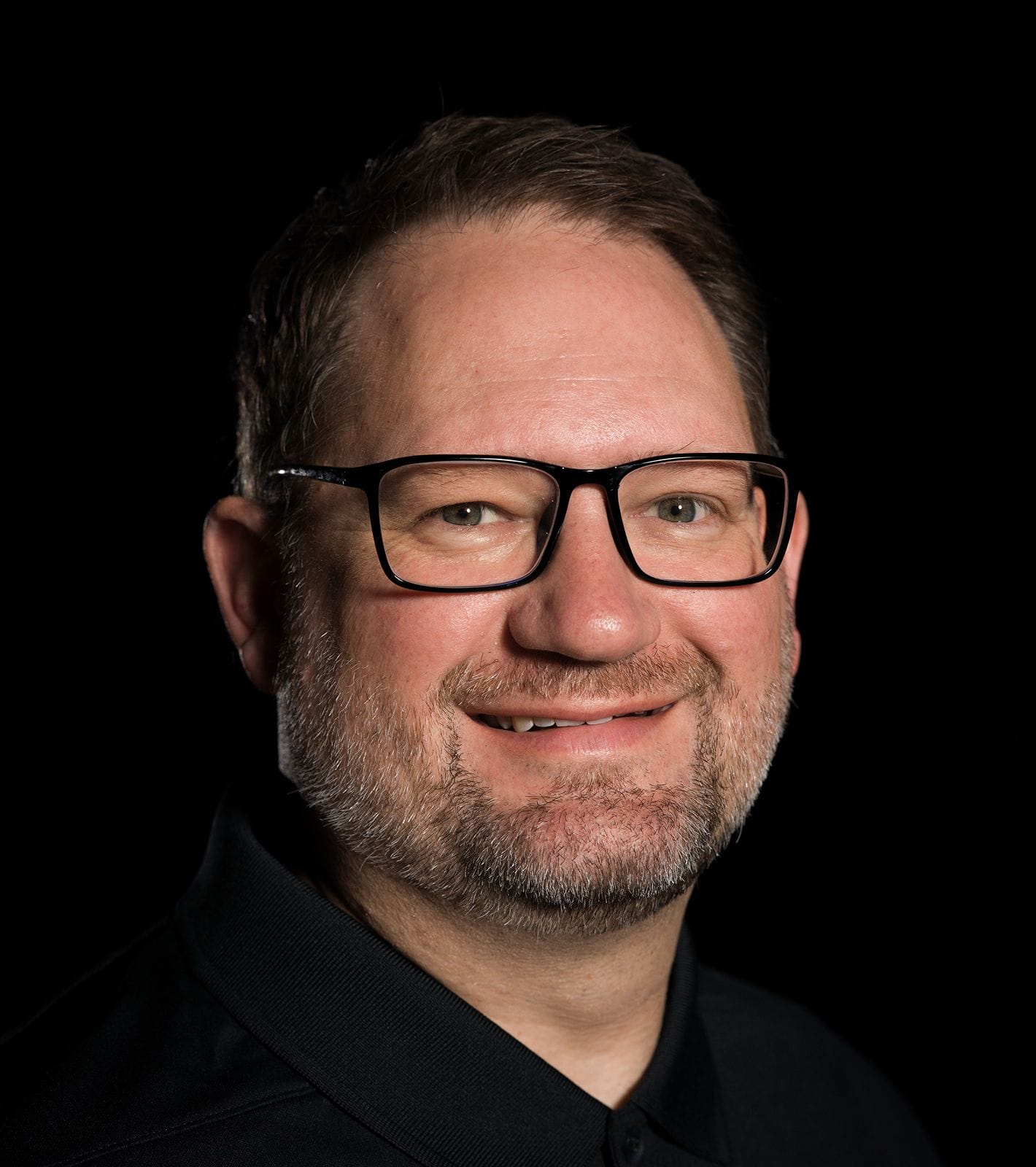 Headshot of a smiling man with glasses and a short beard.