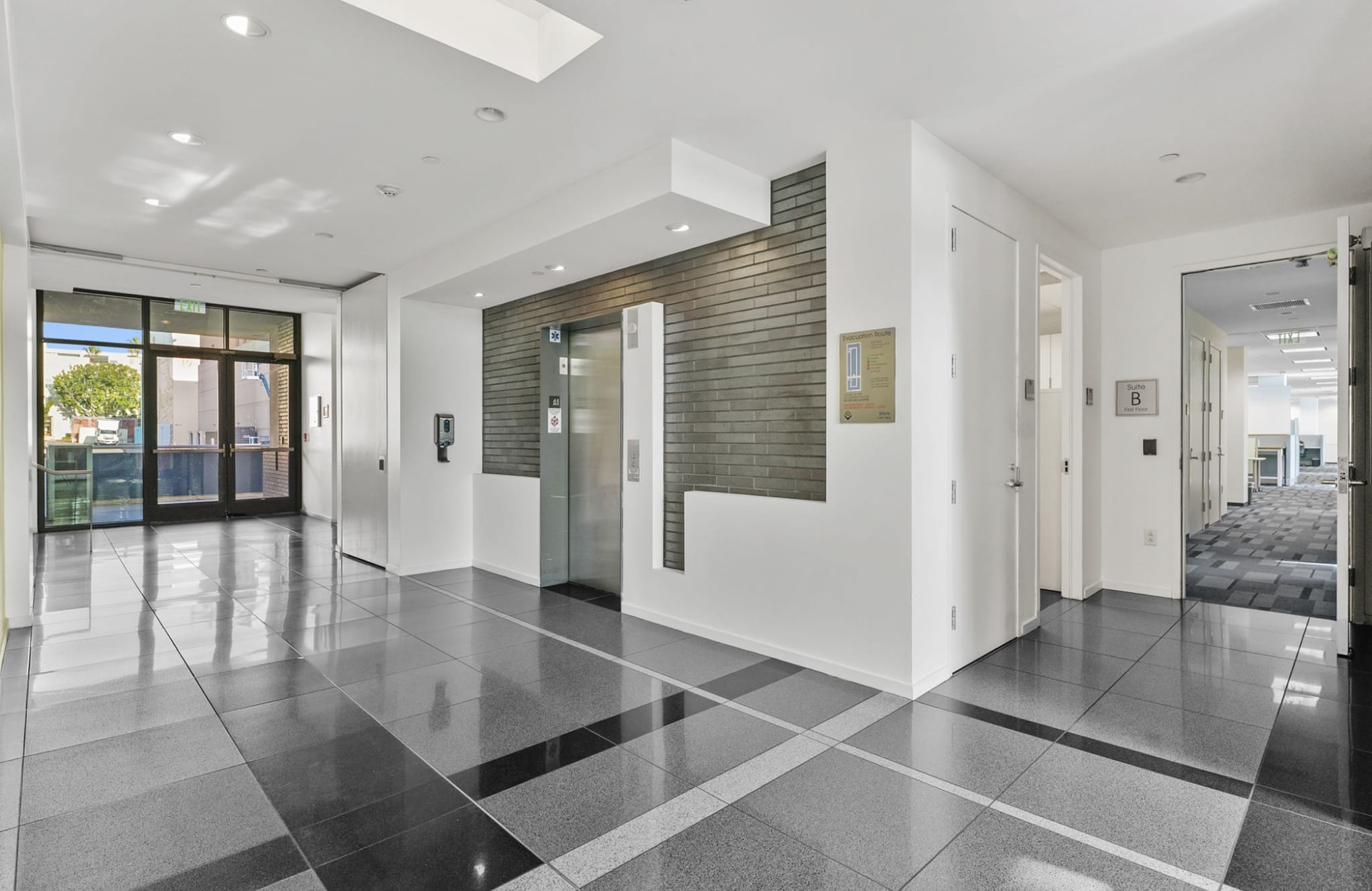 Modern building lobby with shiny dark tiled floors, glass entry doors, and an elevator.