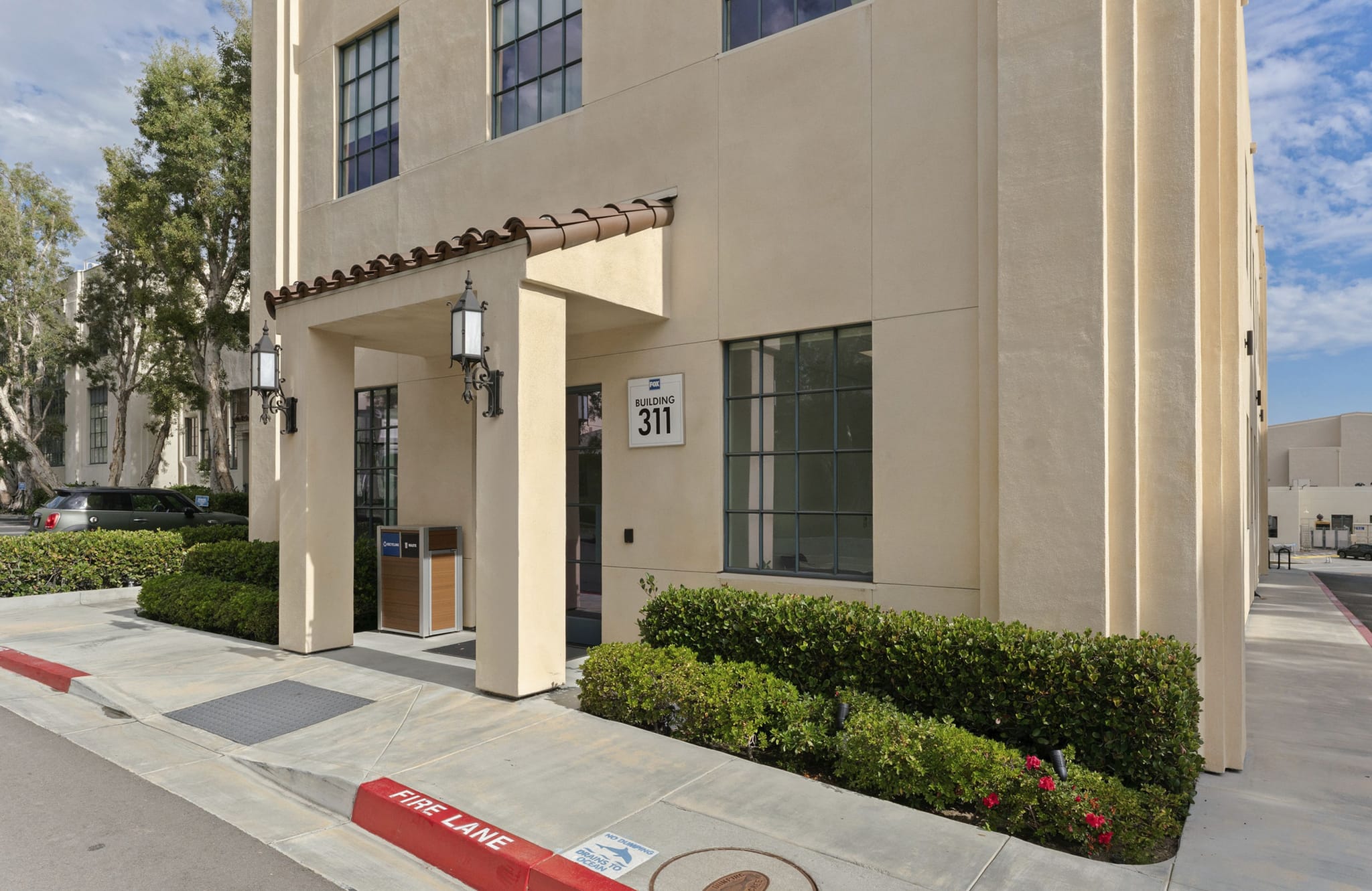 Exterior of a cream-colored building entrance with a tiled canopy, showing "BUILDING 311" and green bushes.