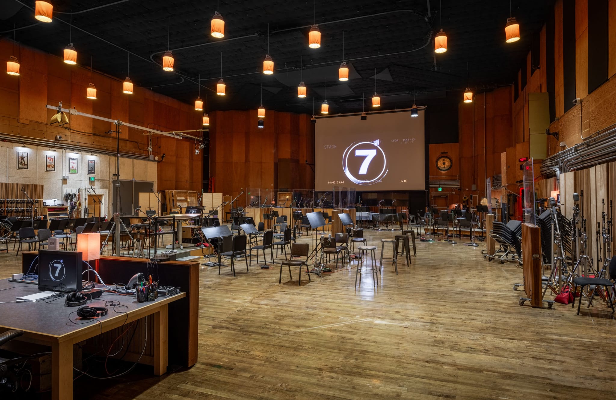 Orchestral recording studio with chairs, music stands, microphones, and a screen showing a large number 7.