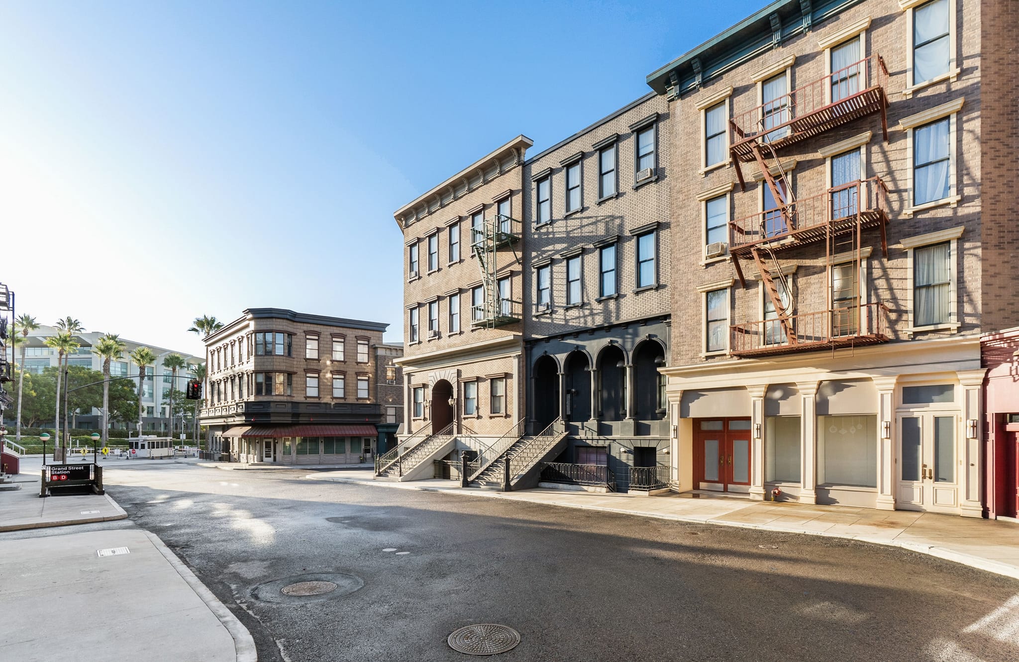An empty city street lined with old-style brick buildings, many with fire escapes, under a clear blue sky.