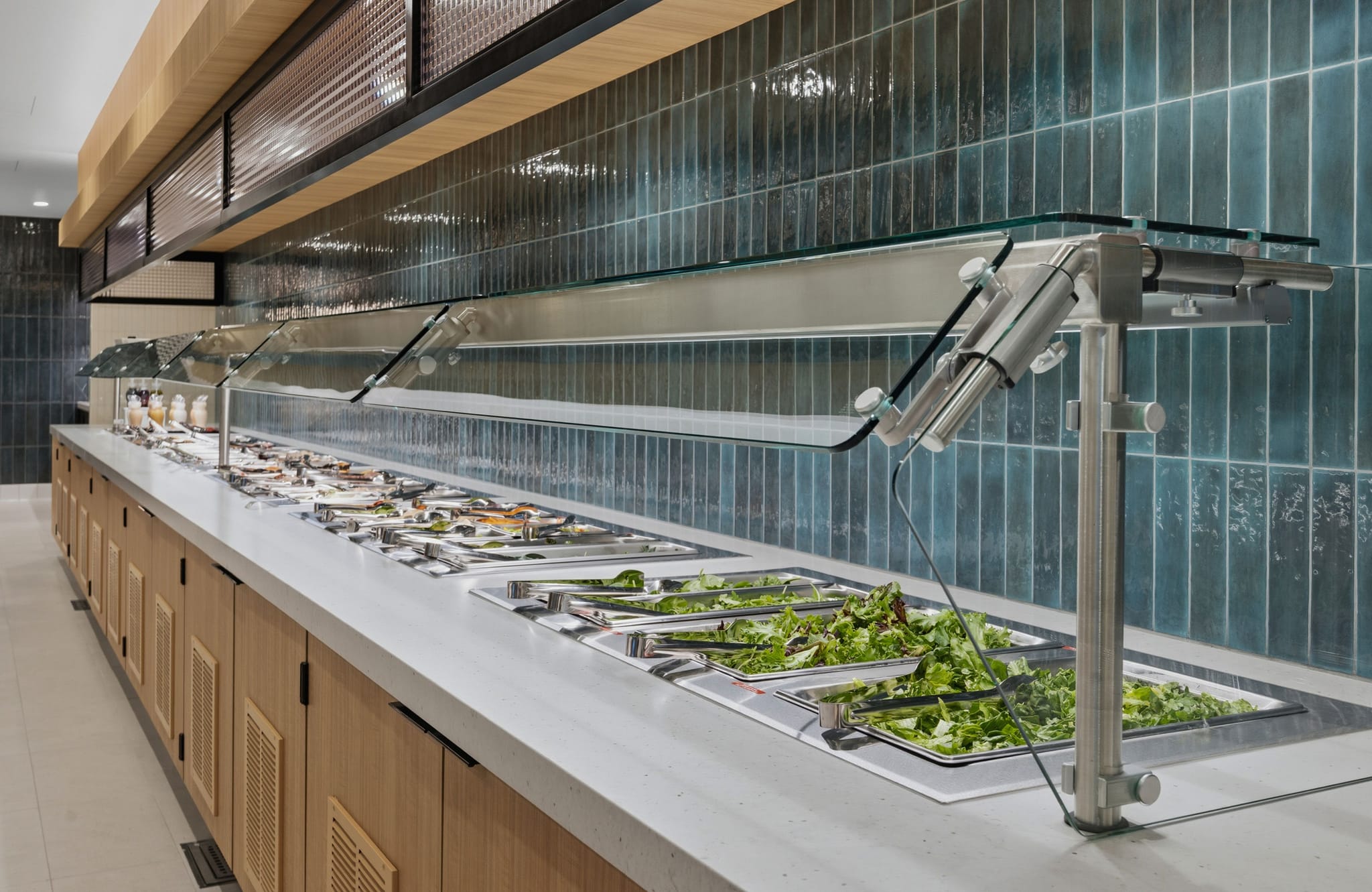 Long self-service food bar with various dishes, including salad, under glass sneeze guards.