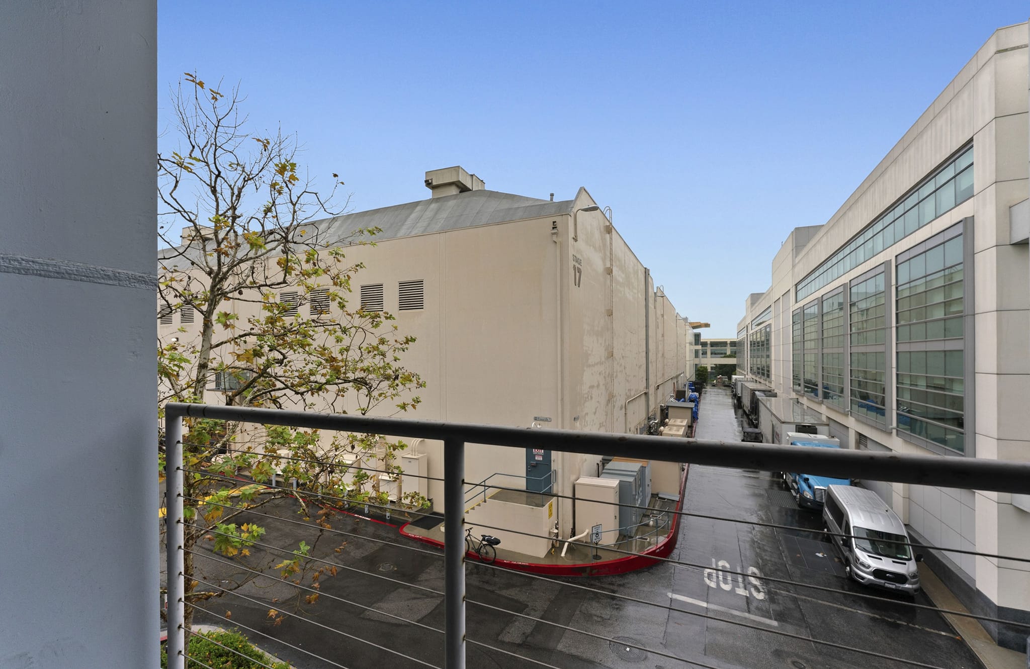 View from a balcony showing a wet alleyway between two large buildings with a tree and a parked van.