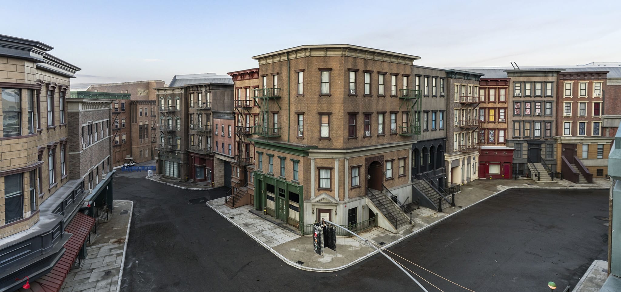 An empty intersection in a city, flanked by multi-story buildings with fire escapes.