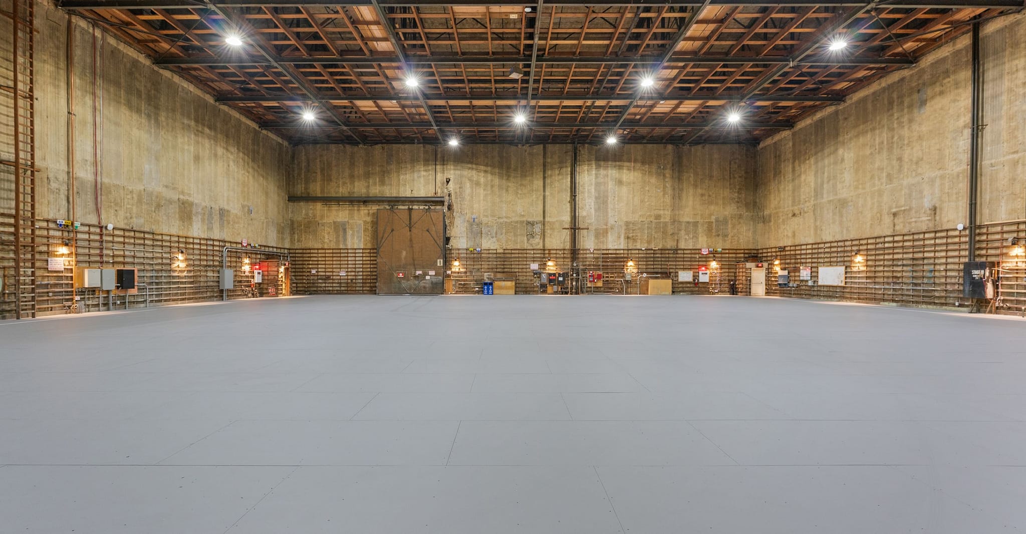 Empty sound stage with a gray floor, industrial walls, and a high exposed beam ceiling.