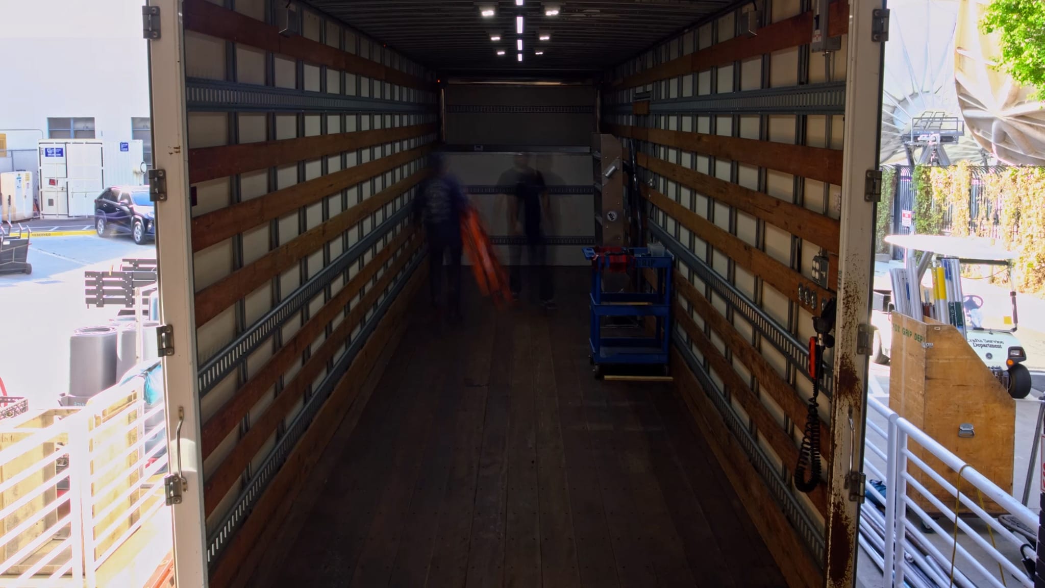 Interior view of an empty truck trailer looking out, with blurred figures visible inside.