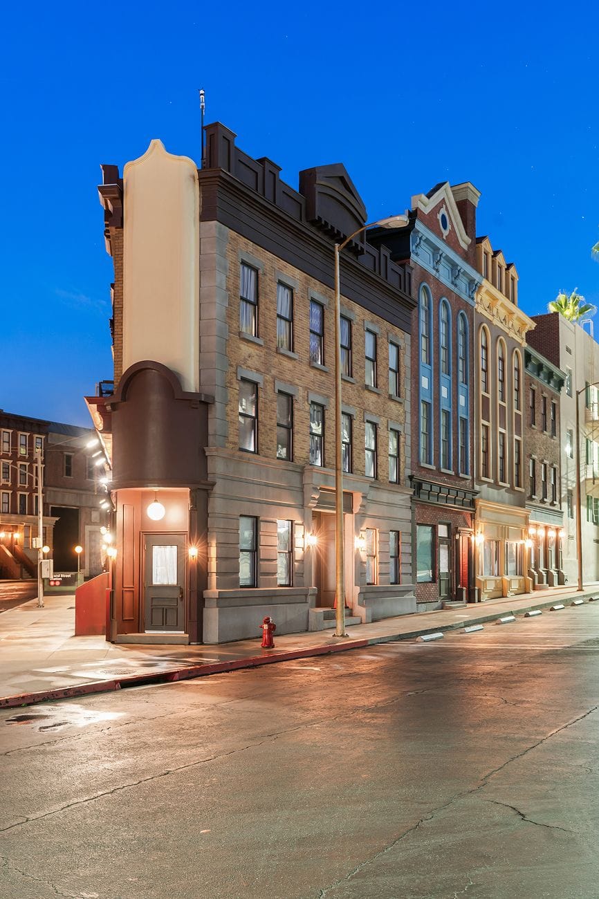 A wet street at dusk lined with multi-story historic buildings, their lights reflecting on the pavement.