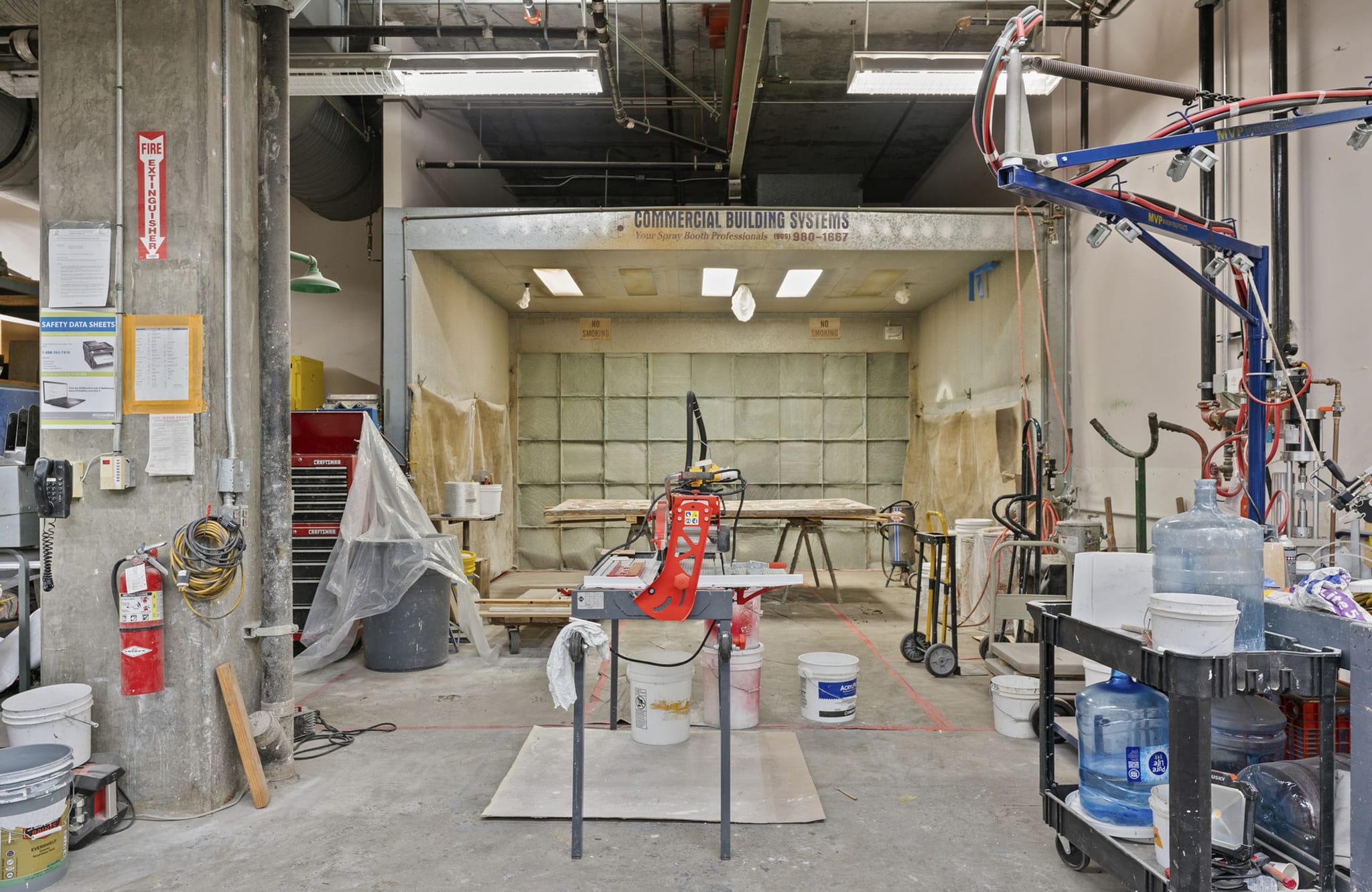 A functional industrial workshop with a large spray booth, various tools, and supplies.