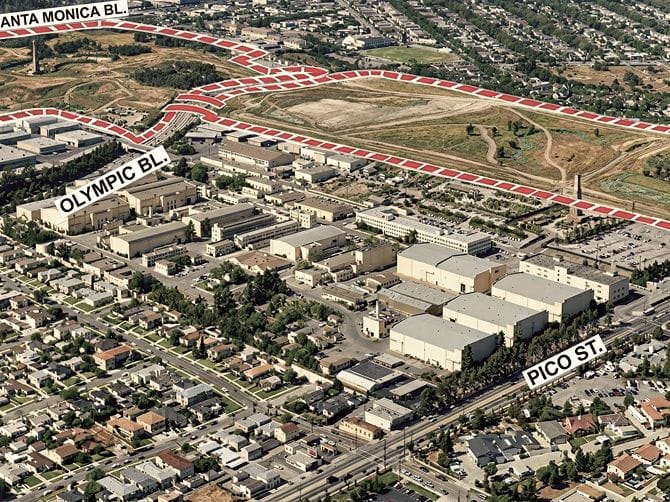 Aerial view of an urban landscape with a large studio complex, residential neighborhoods, and open undeveloped land. Santa Monica, Olympic, and Pico Boulevards are labeled.