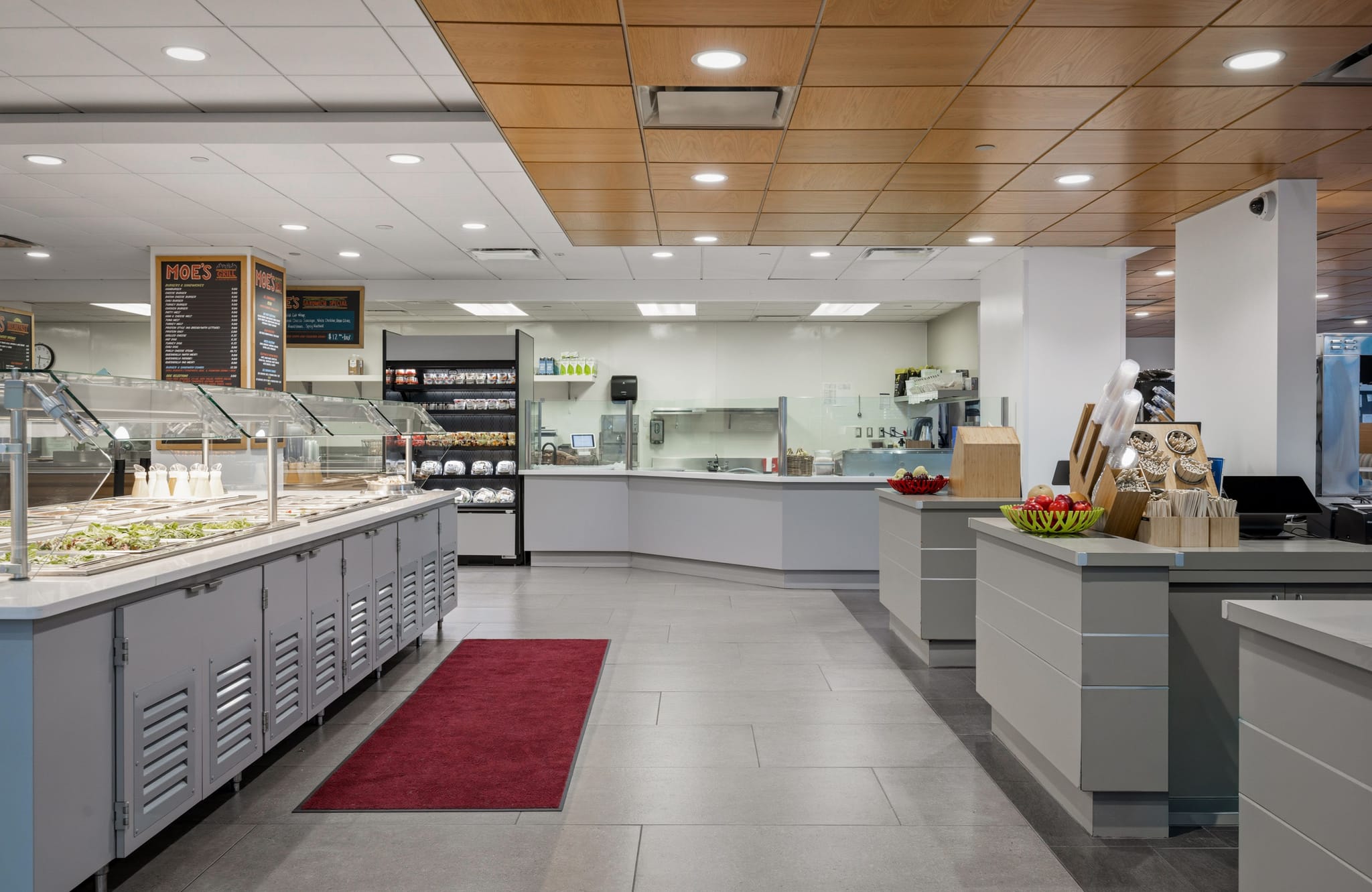 A modern cafeteria interior featuring a salad bar, grab-and-go selections, and checkout counters.
