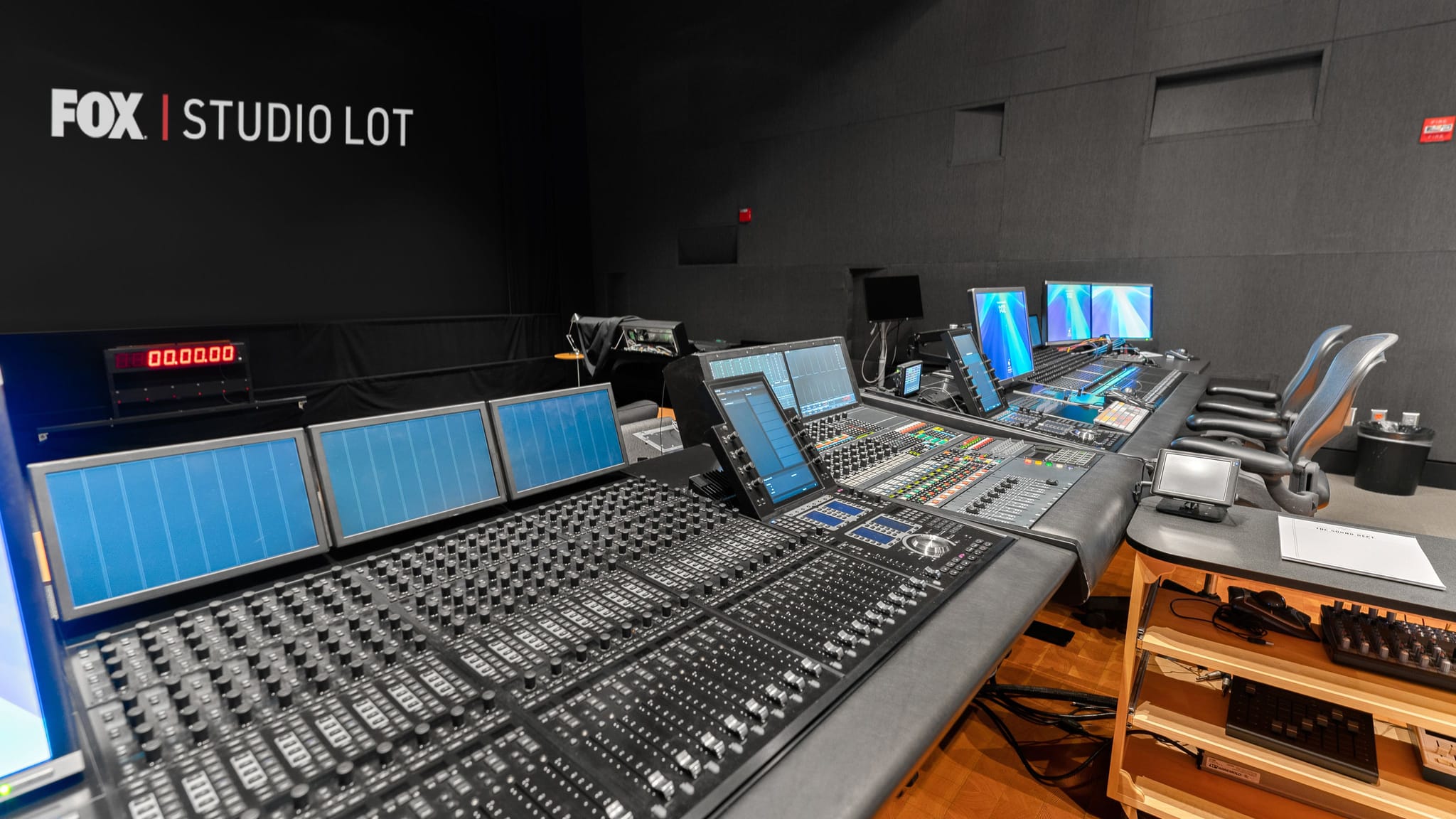 A professional audio mixing console with multiple screens and a digital timer in a FOX Studio Lot control room.