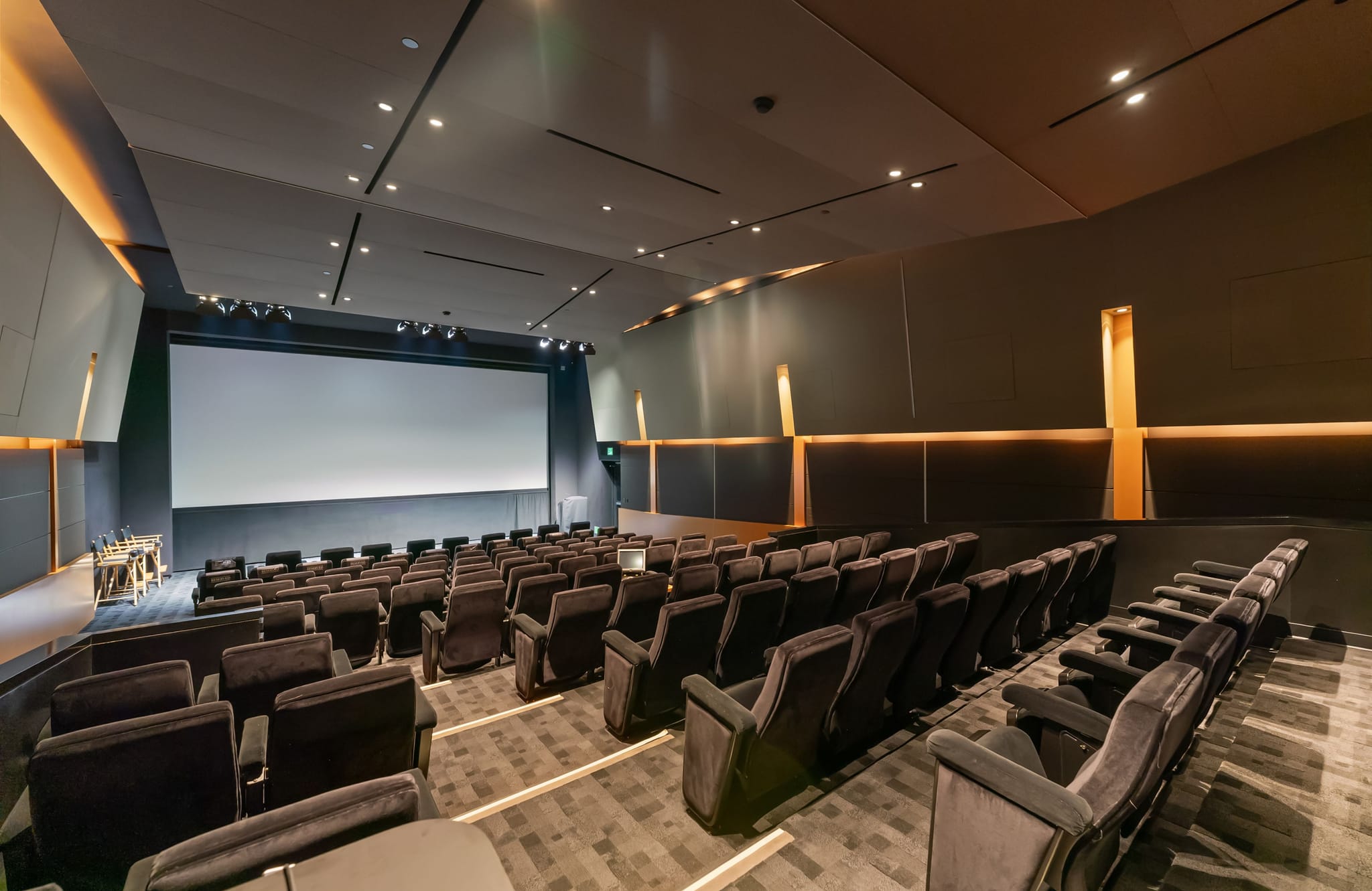 A modern, empty cinema with a large blank screen, rows of dark seating, and warm accent lighting.