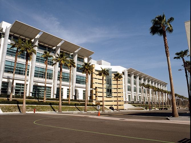 Modern building with white roof overhangs and palm trees lining a street.