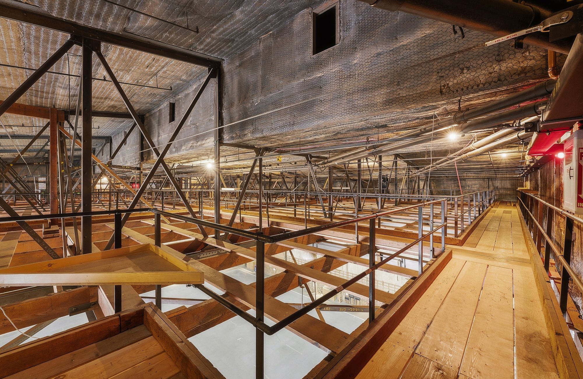 An industrial interior featuring multi-level wooden platforms, metal railings, and an exposed concrete ceiling.