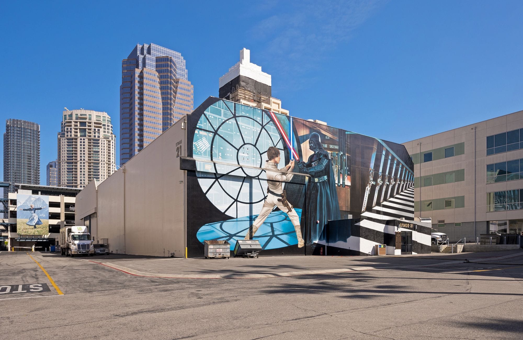 A building in a city featuring a mural of Luke Skywalker and Darth Vader lightsaber dueling, against a circular window and striped hallway.