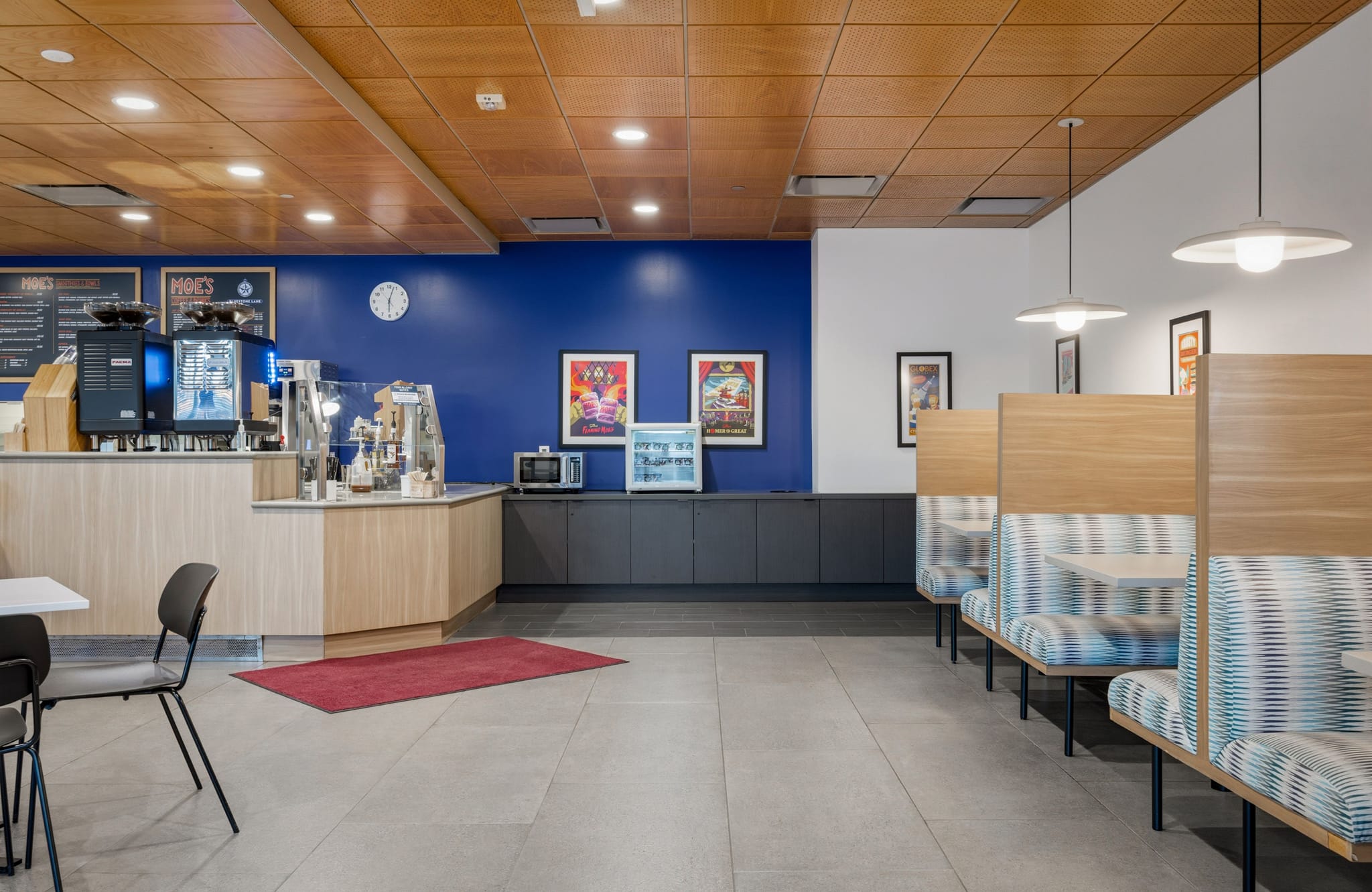 A modern cafe interior with a counter, espresso machines, a blue accent wall with art, and striped booth seating.