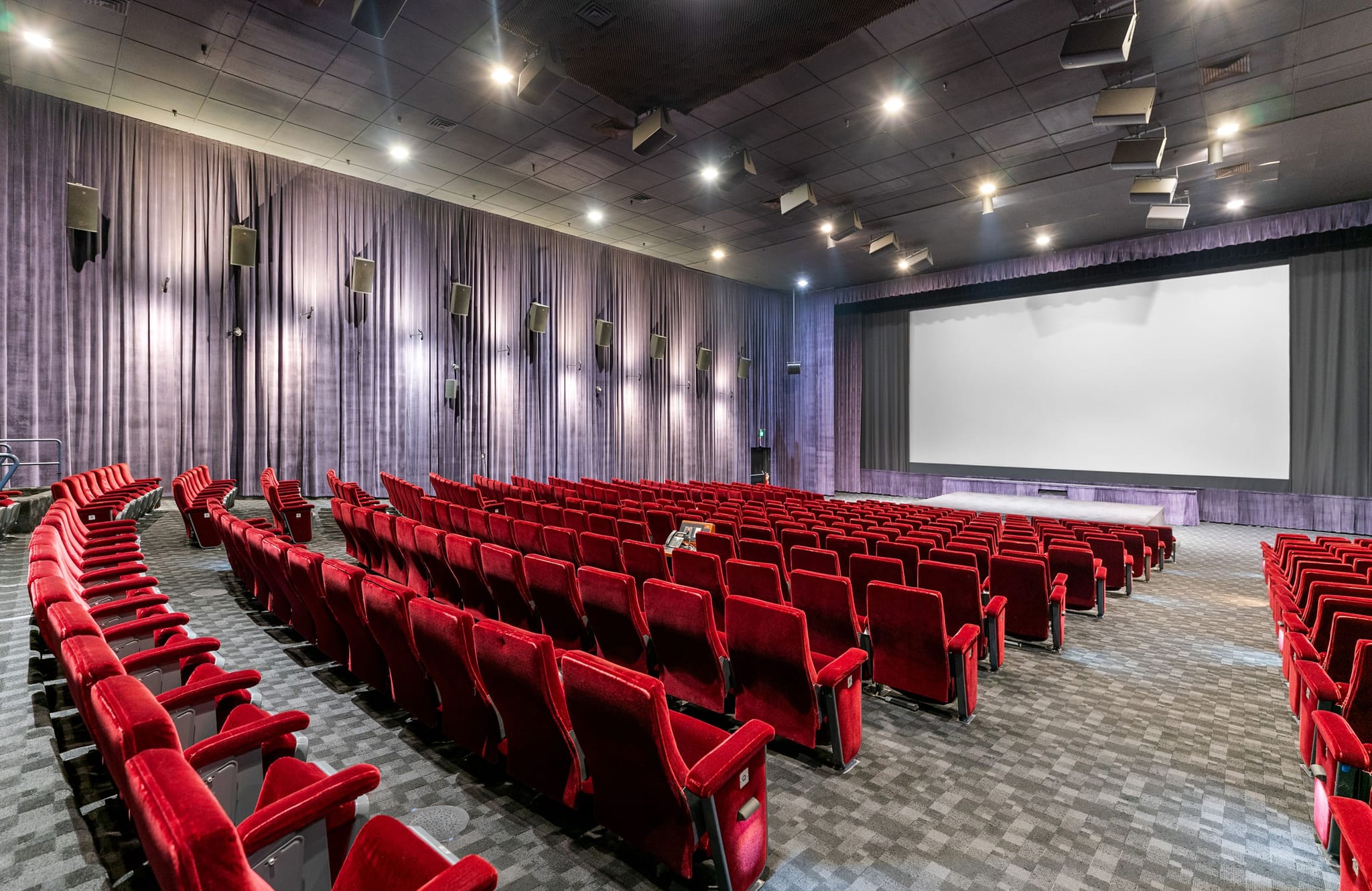 Empty movie theater with rows of red seats and a large screen.