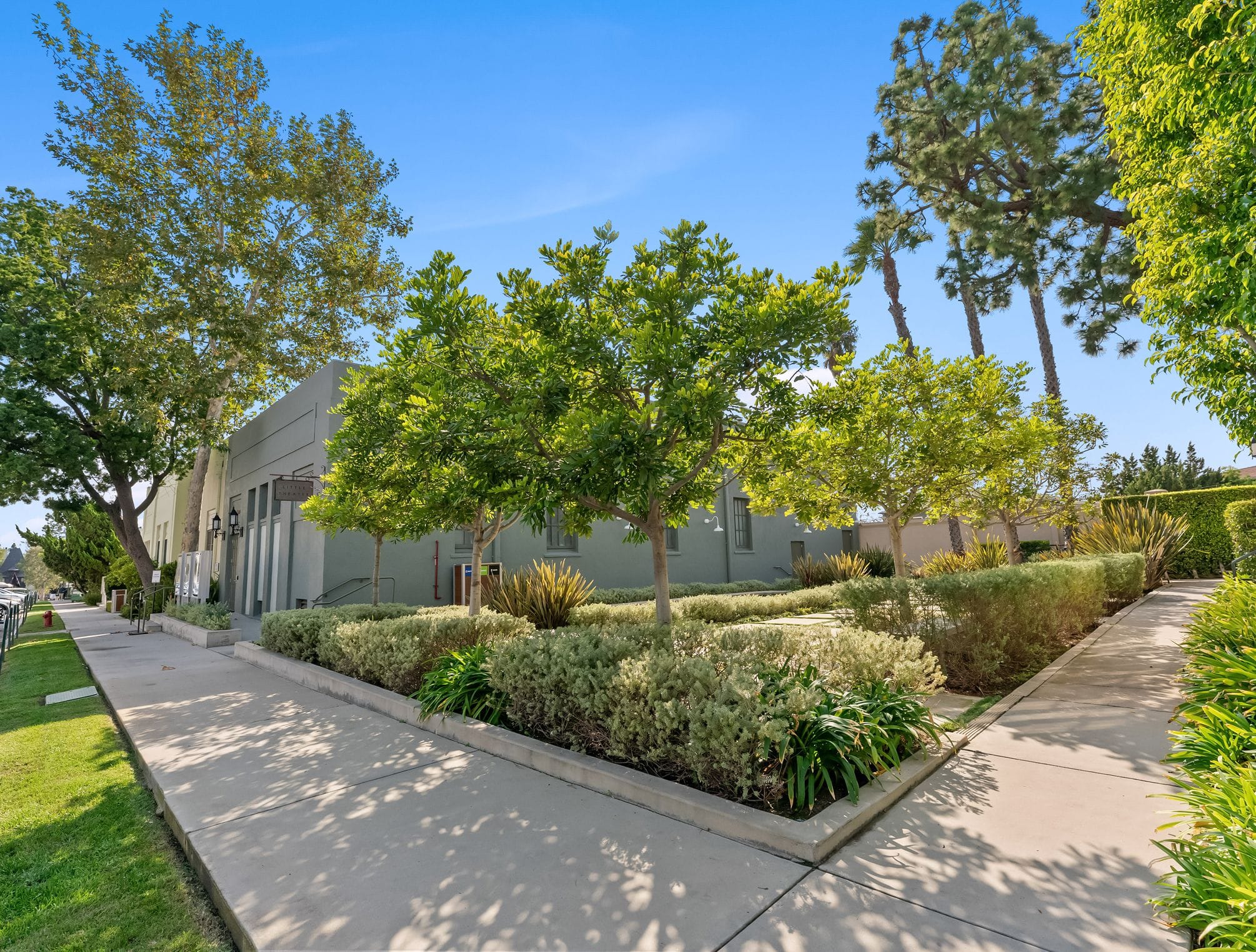 Modern grey building with a sidewalk and neatly landscaped garden under a clear blue sky.