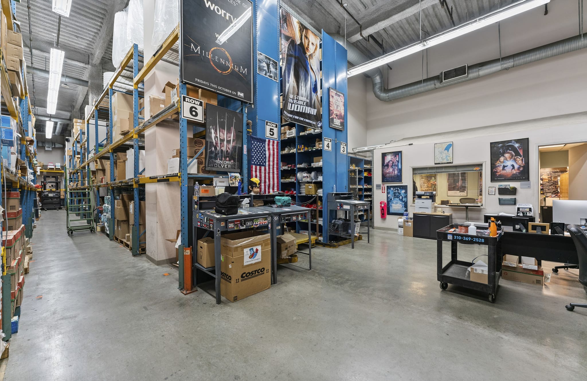 A large room with tall warehouse shelves on the left and an office area with desks and movie posters on the right.