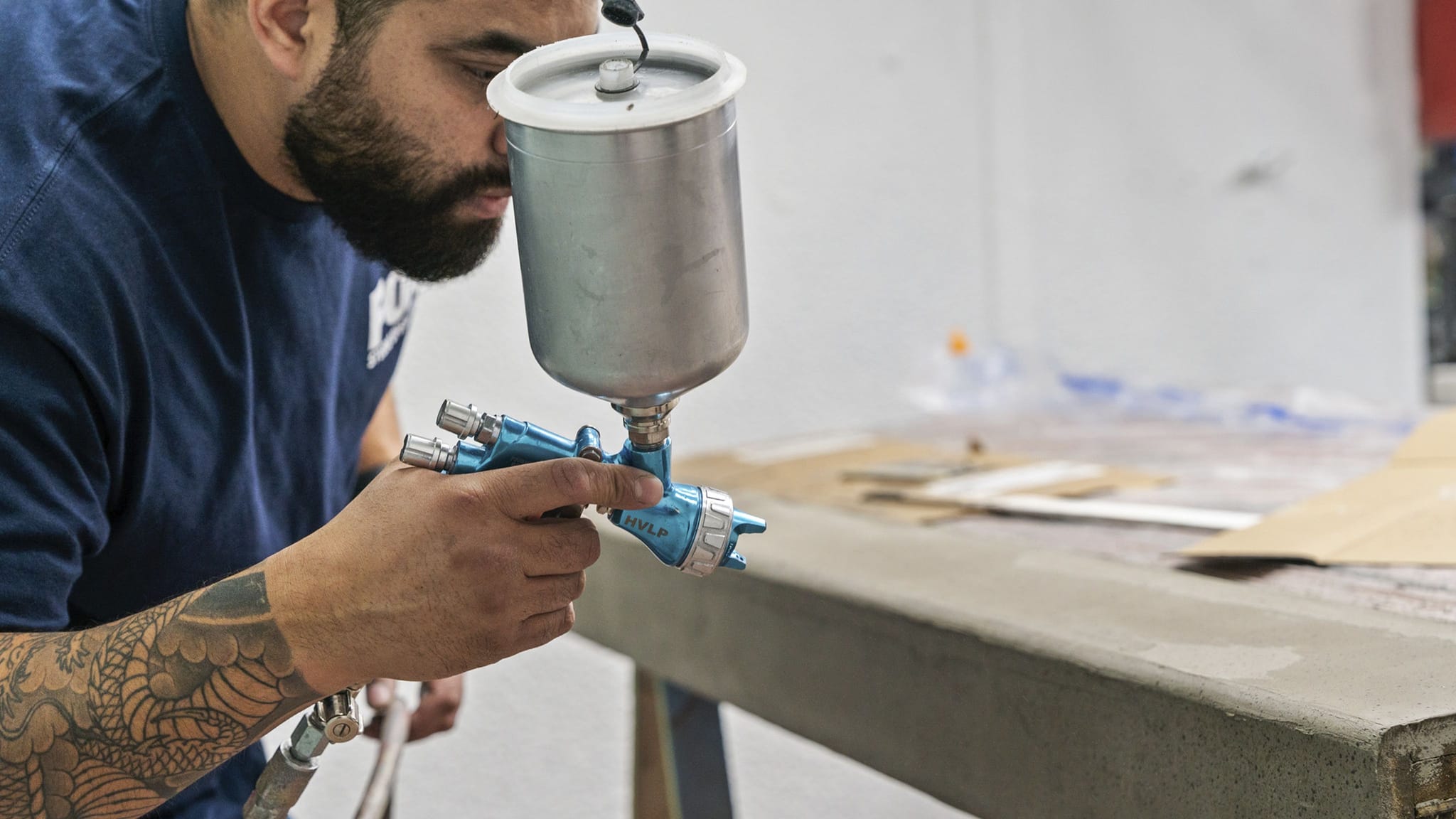 A bearded man with a tattooed arm spray painting.