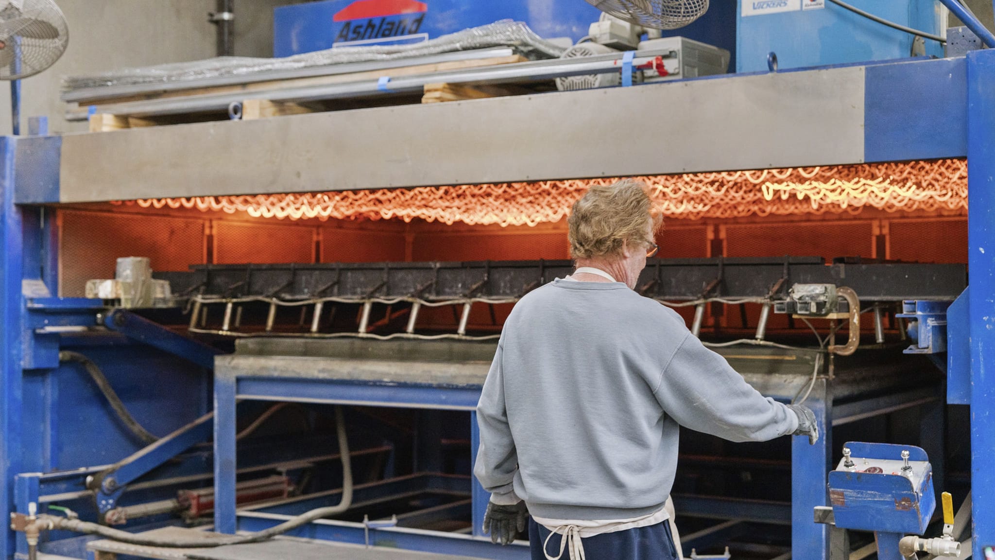 Worker monitoring a large industrial oven with glowing heating elements and molds inside.