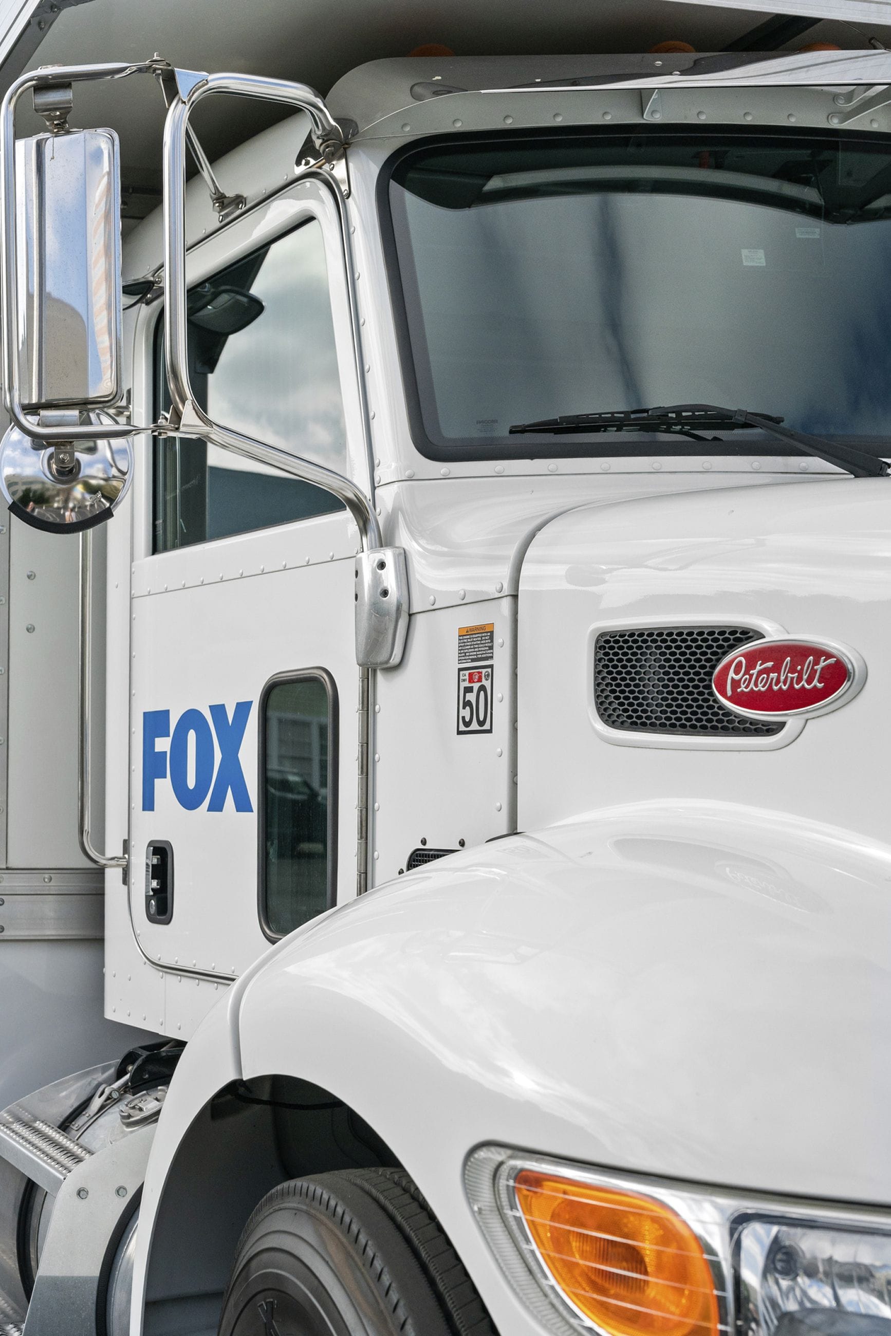 Front-quarter view of a white Peterbilt semi-truck with a blue "FOX" logo on its cab.
