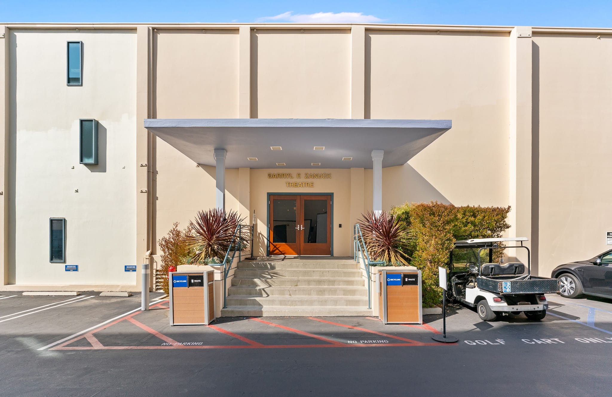 Exterior of the Carroll C. and Charlotte T. Thornton Theatre, a tan building with a covered entrance, steps, and a golf cart parked in the foreground.