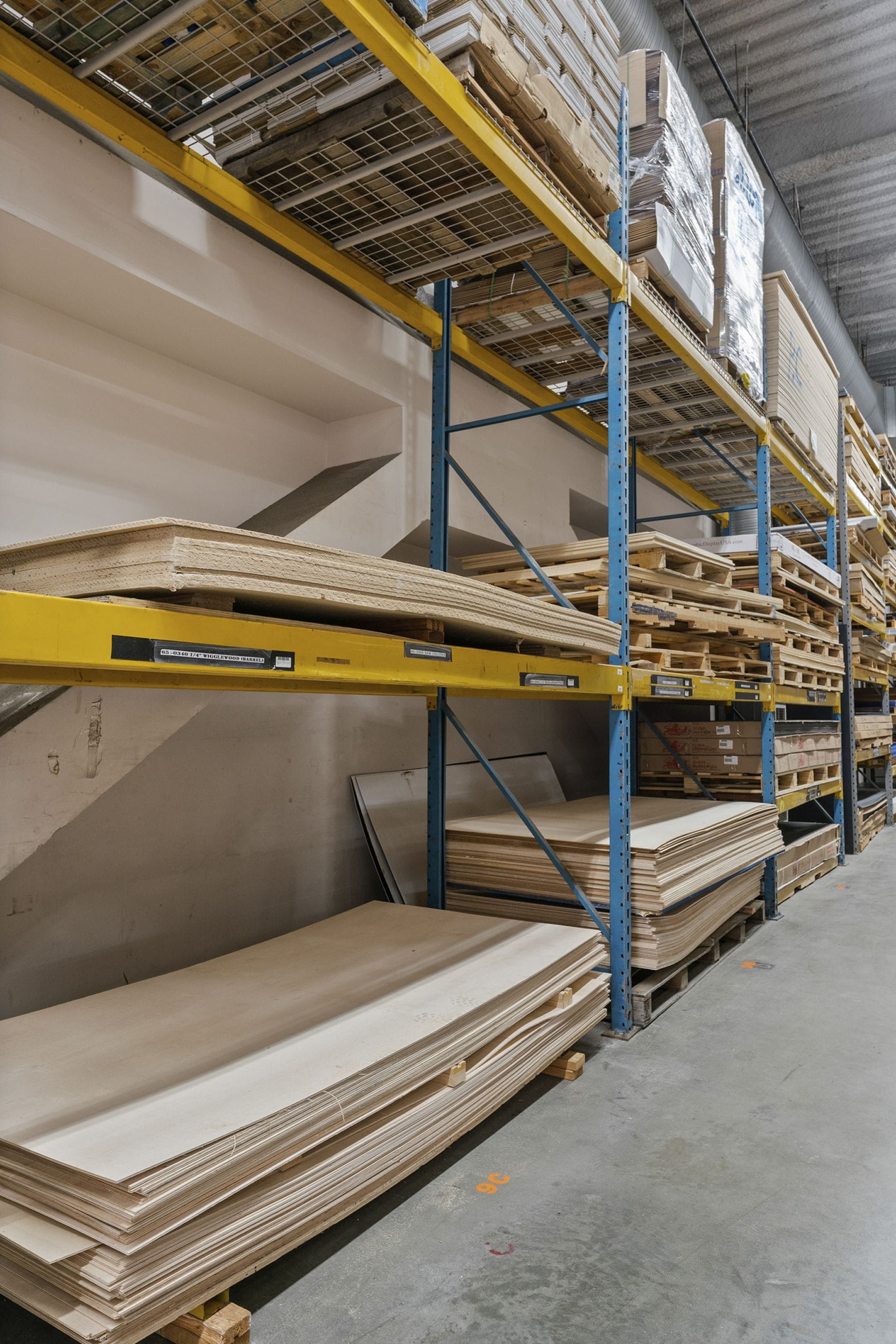 A warehouse aisle with stacked wooden sheets on tall metal shelves and the floor.