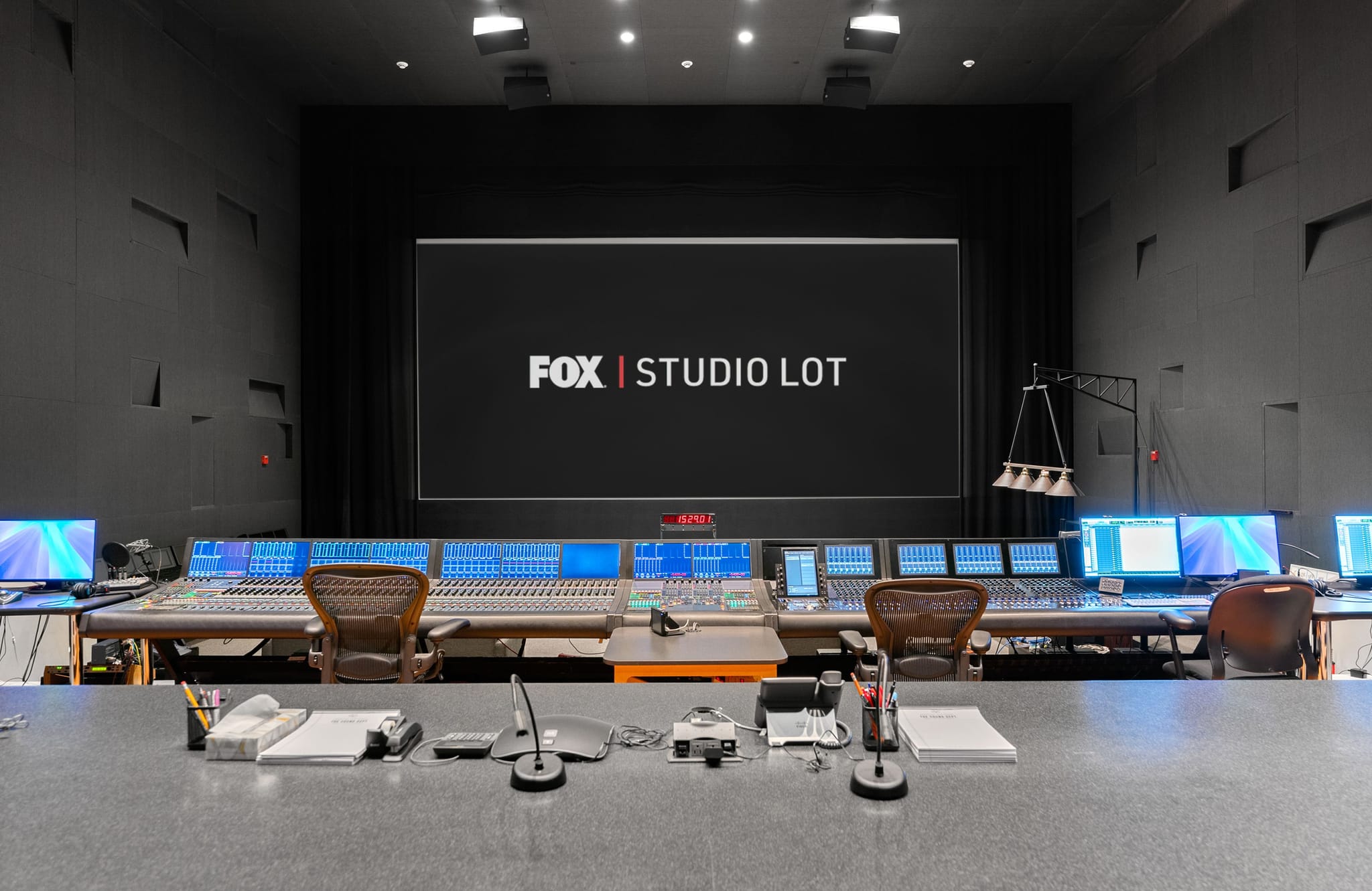 A modern broadcast control room with multiple mixing consoles, computer screens, and a large display showing "FOX | STUDIO LOT".
