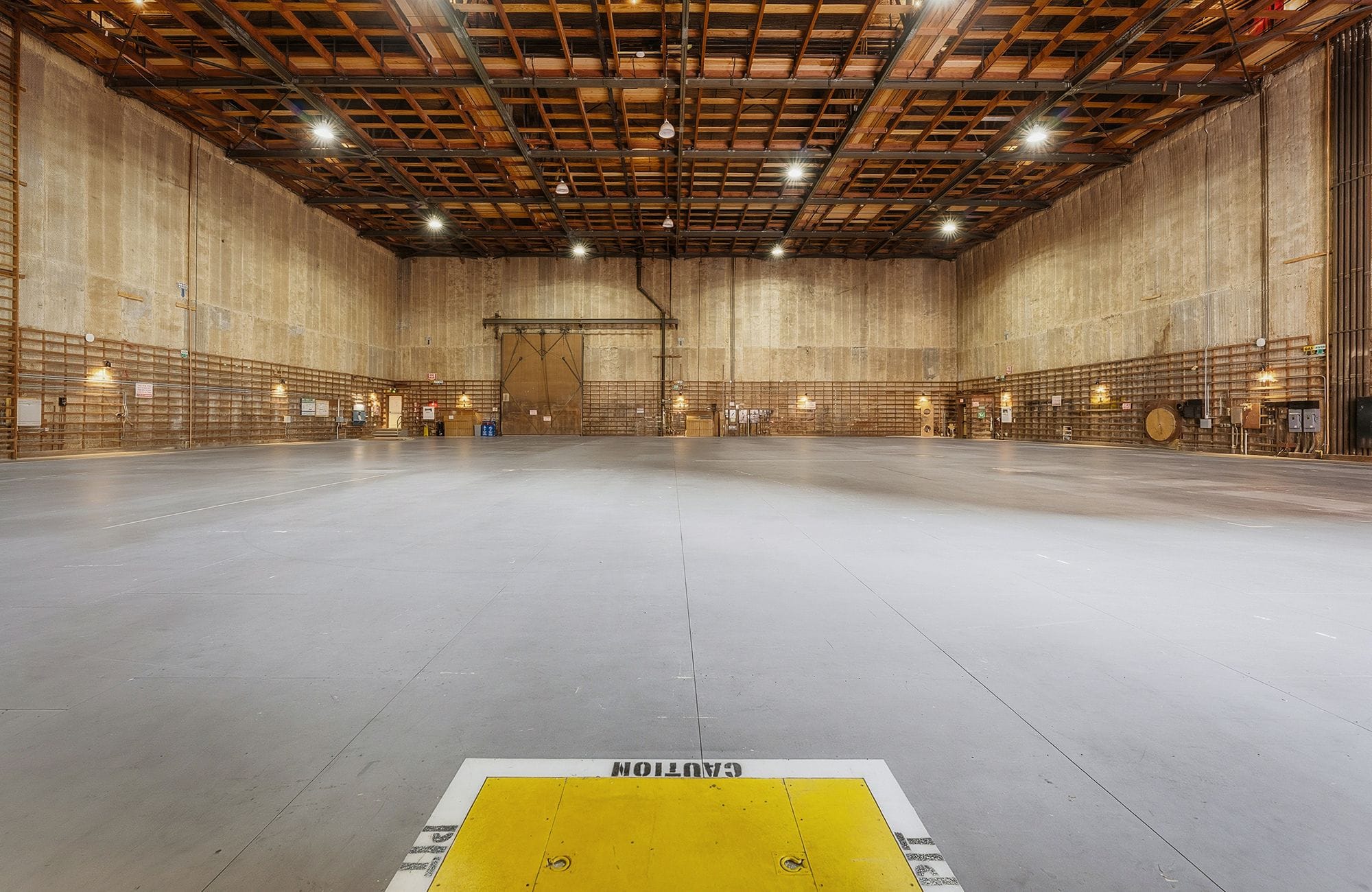 A large, empty industrial warehouse with a concrete floor and exposed wooden ceiling.