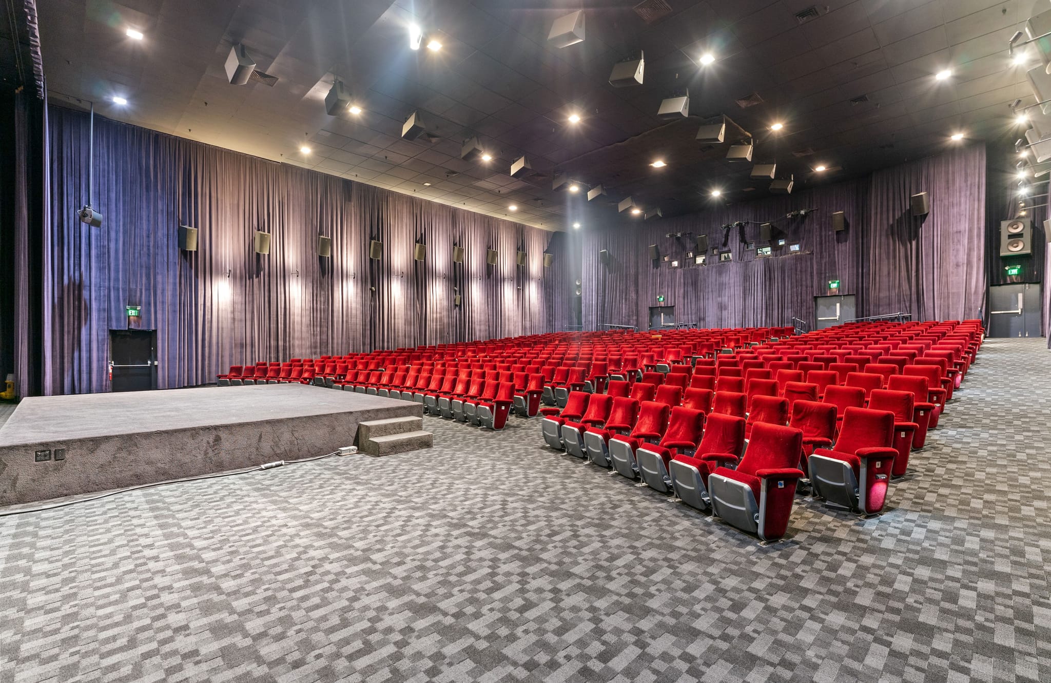 Empty auditorium with a stage, rows of red seats, and dark curtains.